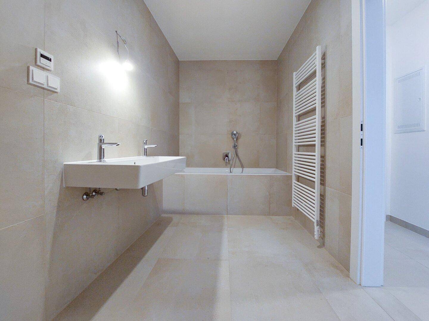 Modernes Badezimmer mit beigefarbenen Fliesen, Badewanne und beheiztem Handtuchhalter.