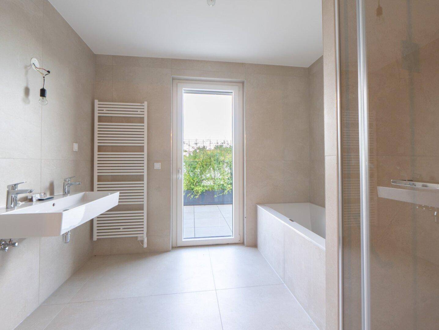 Modernes Badezimmer mit Doppelwaschbecken, Badewanne, Dusche und Zugang zur Terrasse.