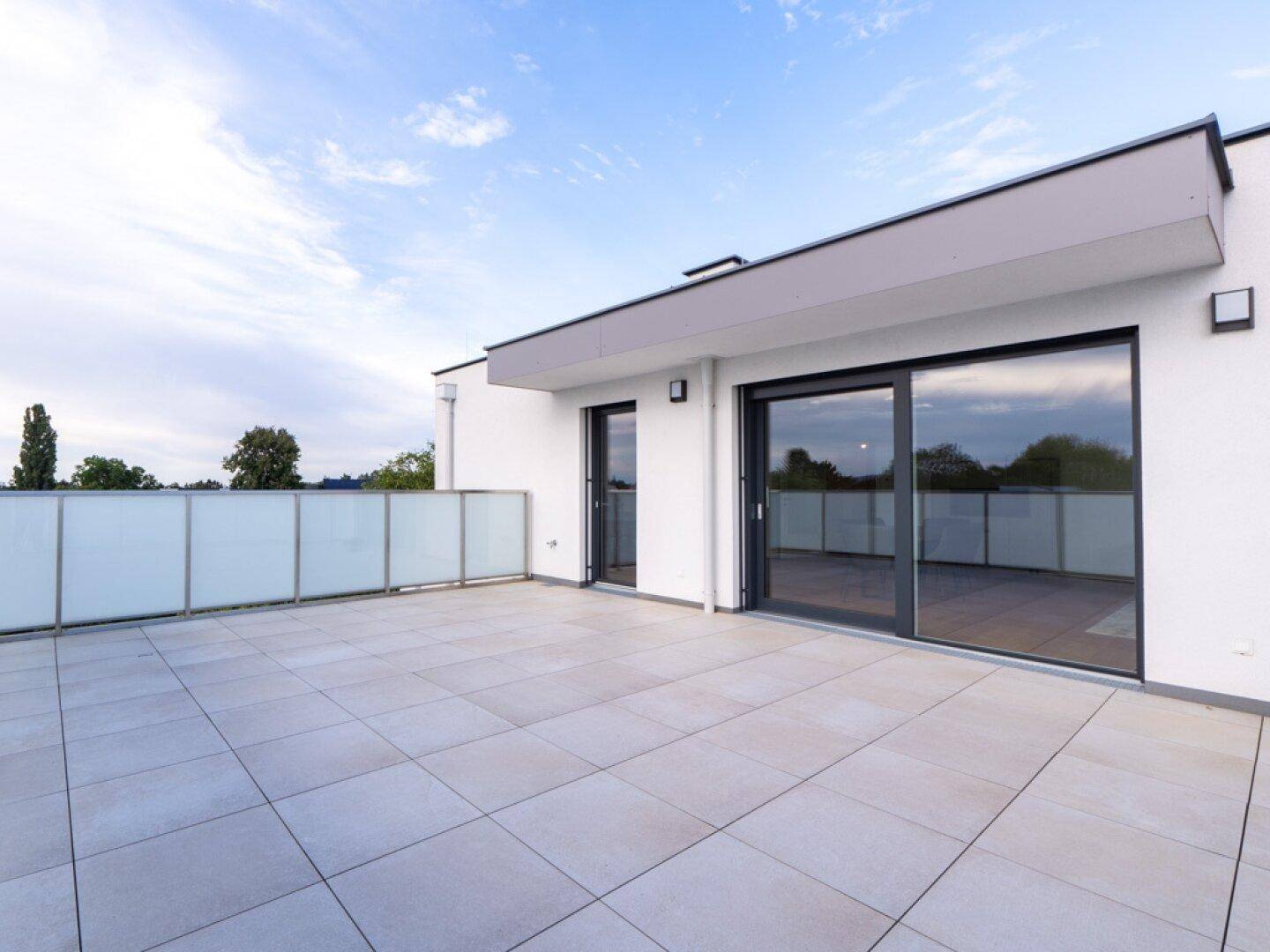 Großzügige Dachterrasse mit moderner Architektur, Fliesenboden und weitem Himmelblick.