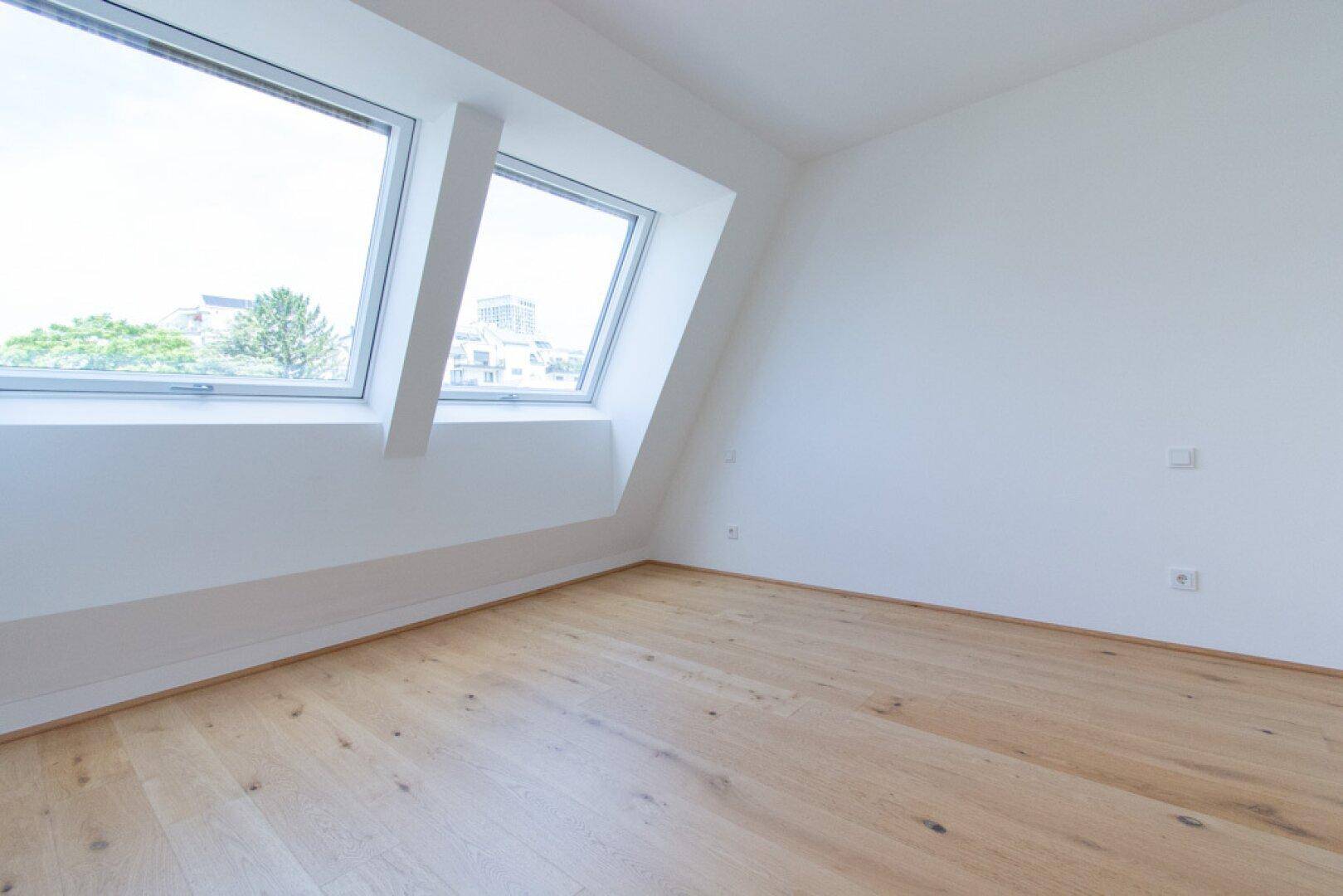 Dachgeschosszimmer mit viel Tageslicht durch große Dachfenster und hellem Holzboden.