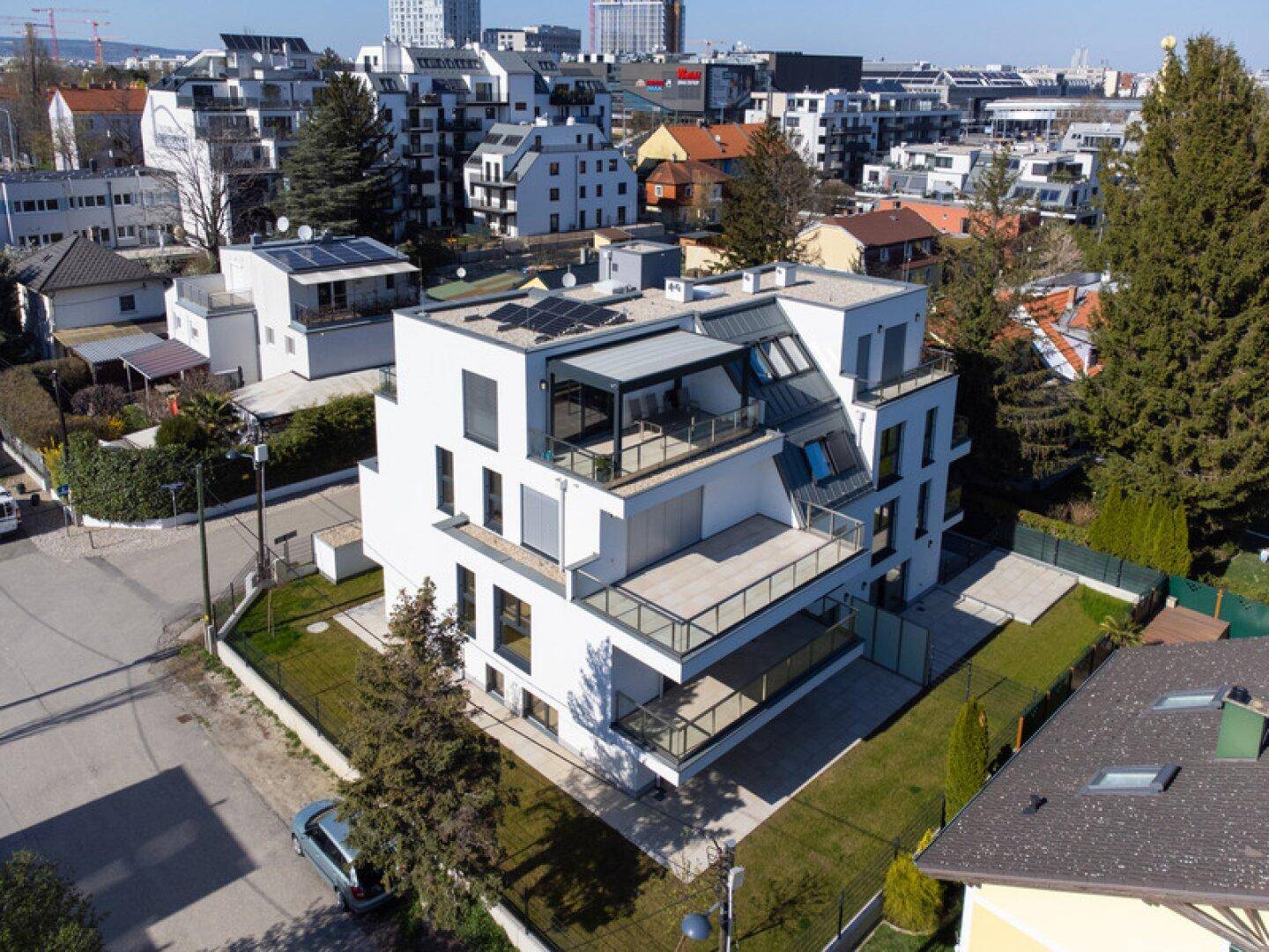 Moderne Wohnanlage mit Flachdach, Balkonen und Photovoltaikanlage in städtischer Umgebung.