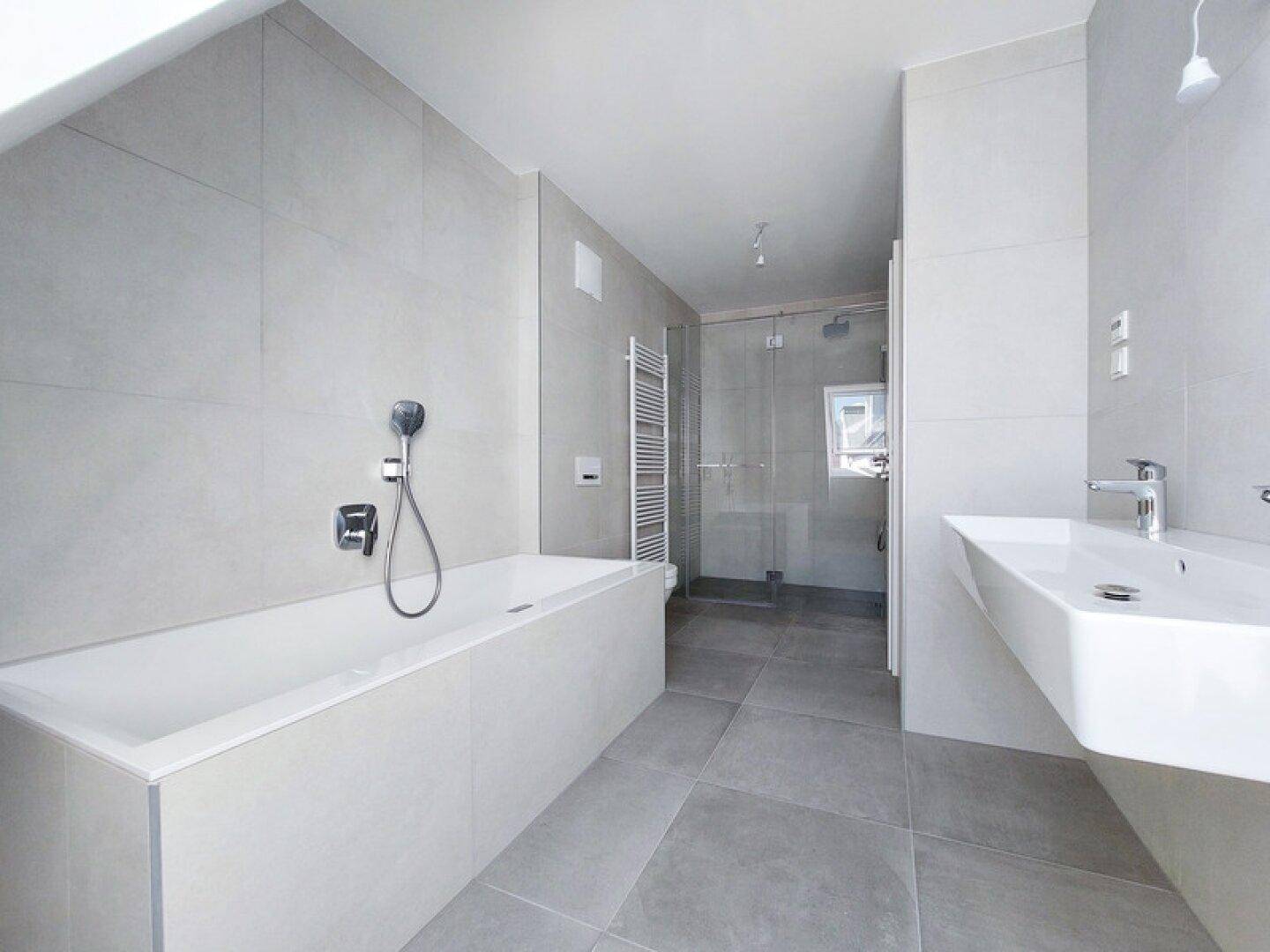 Modernes Badezimmer mit Badewanne, ebenerdiger Dusche und großformatigen grauen Fliesen.
