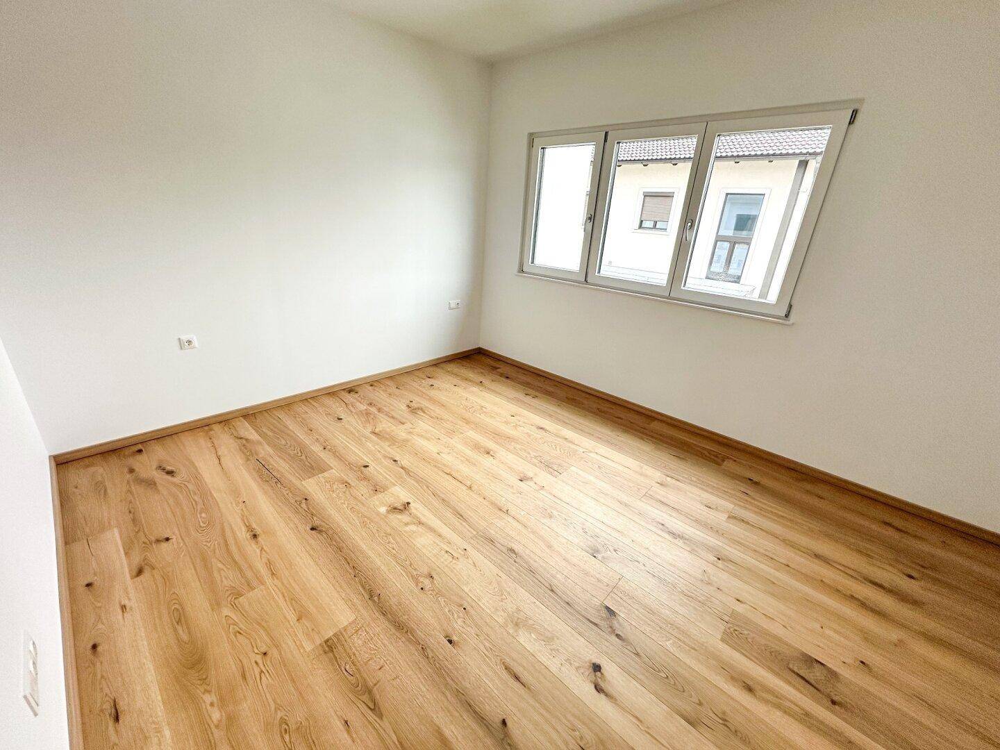 Helles Schlafzimmer mit Holzfußboden und einem Fenster mit Blick auf die Umgebung.