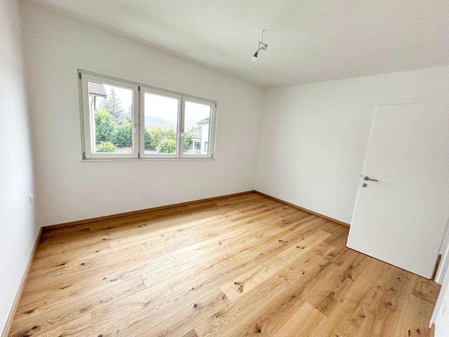 Geräumiges Schlafzimmer mit Holzboden und viel Tageslicht durch das Fenster.