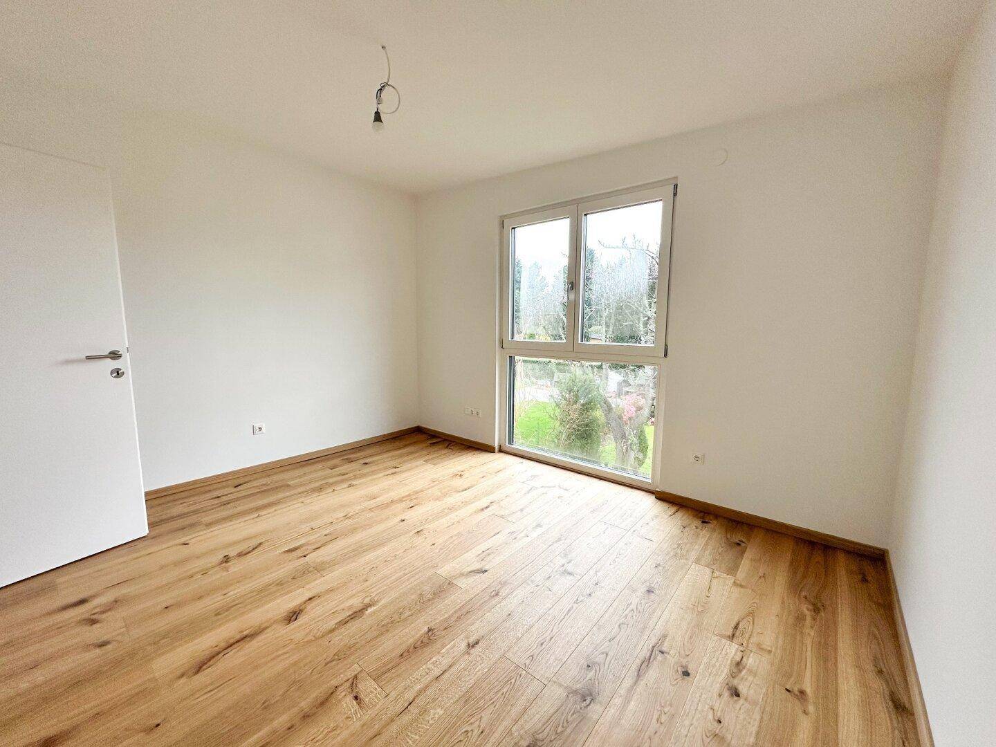 Schlafzimmer mit großem Fenster, Holzboden und Blick ins Grüne.