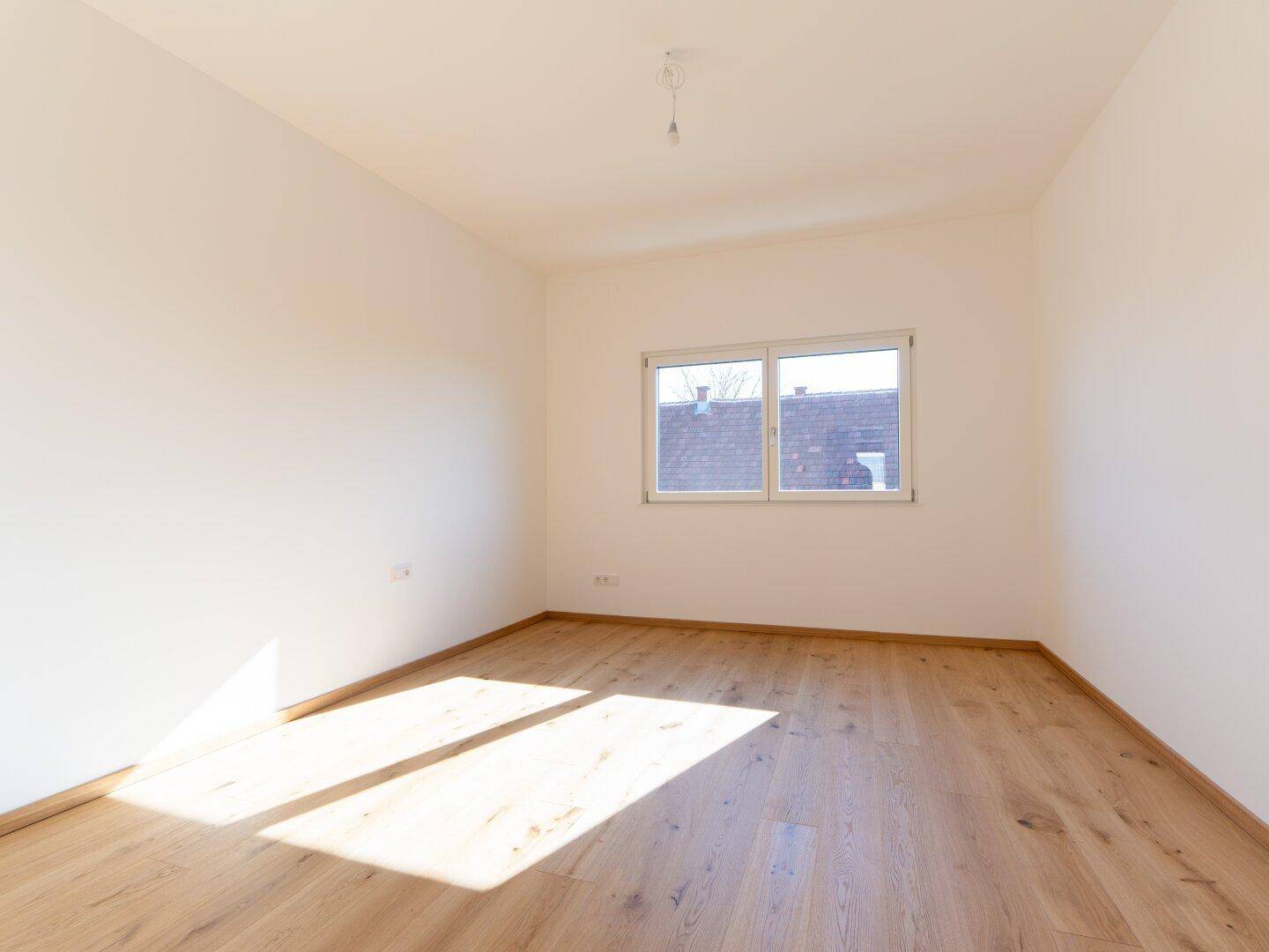 Helles Schlafzimmer mit Eichenparkettboden und einem Fenster, das viel Tageslicht hereinlässt.