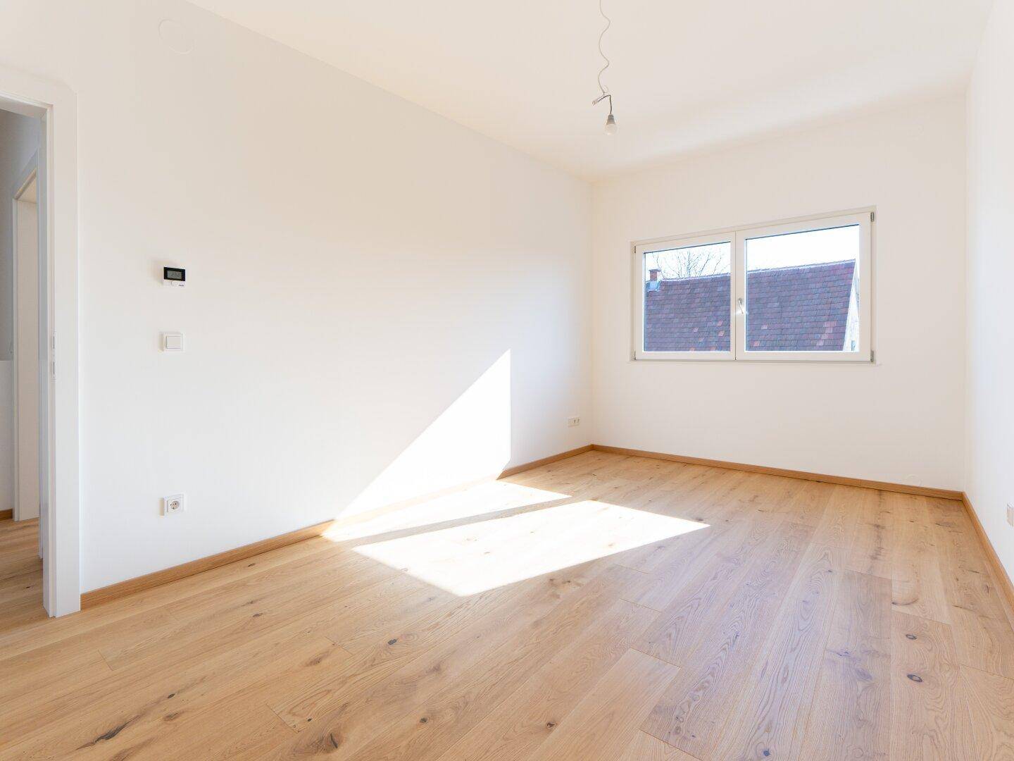 Freundliches Zimmer mit hellem Parkettboden und einem Fenster, das für gute Belichtung sorgt.