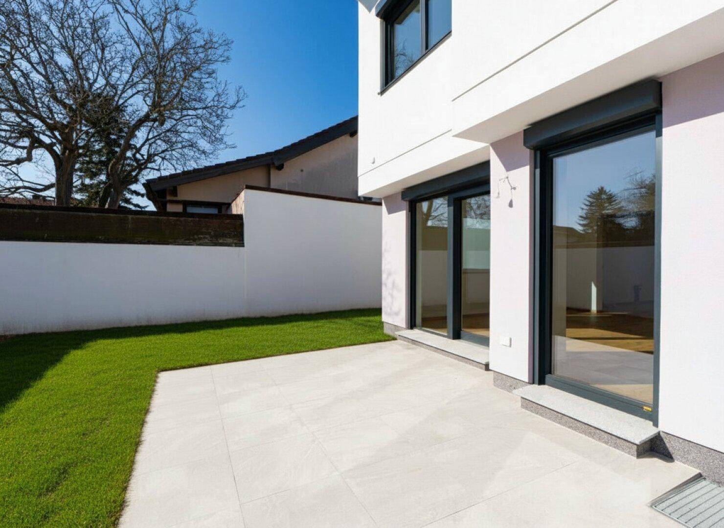 Sonniger Terrassenbereich mit Fliesenboden und angrenzendem Rasen, ideal für Entspannung im Freien.