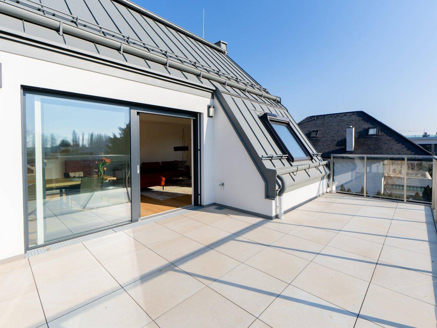 Geräumige Dachterrasse mit Fliesenboden und Zugang zum Innenbereich, umgeben von einem modernen Dach.