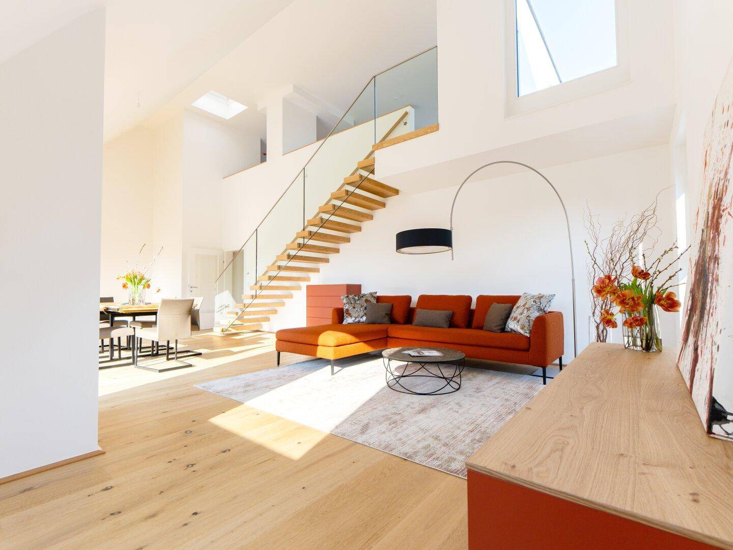 Lichtdurchfluteter Wohnbereich mit hoher Decke, moderner Einrichtung und offener Treppe.