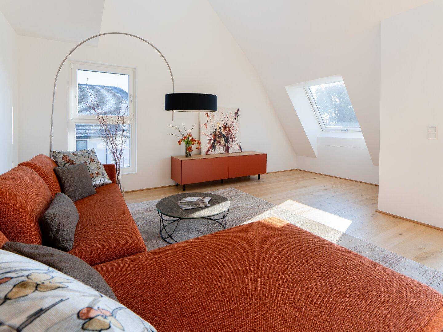 Gemütlicher Wohnbereich mit rotem Sofa, Dachschrägen und großen Fenstern für viel Tageslicht.