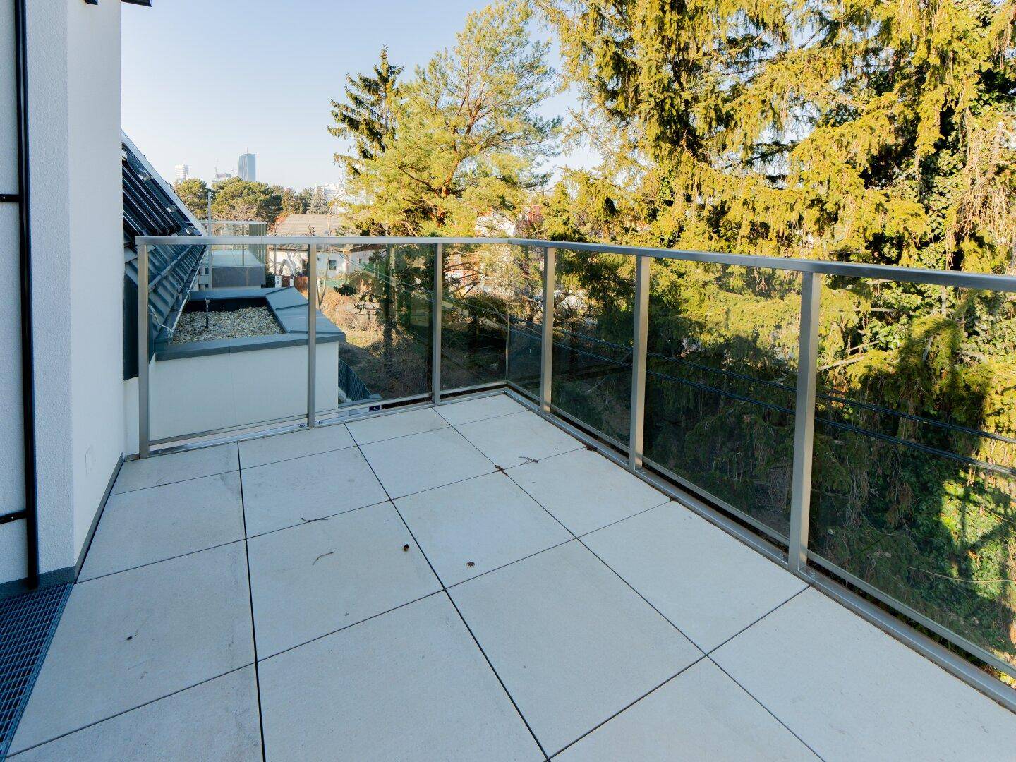 Heller Balkon mit Glasgeländer und Blick ins Grüne sowie auf die Stadt in der Ferne.