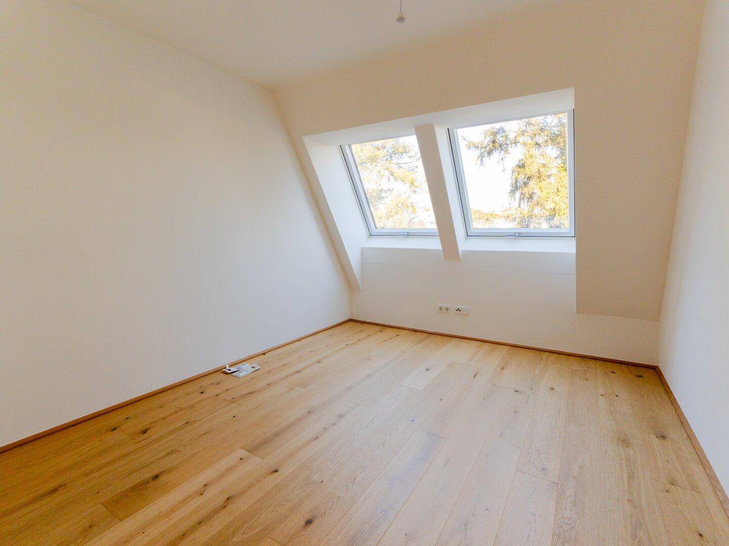 Helles Zimmer mit Dachschrägen, Holzboden und zwei Dachfenstern für natürliches Licht.
