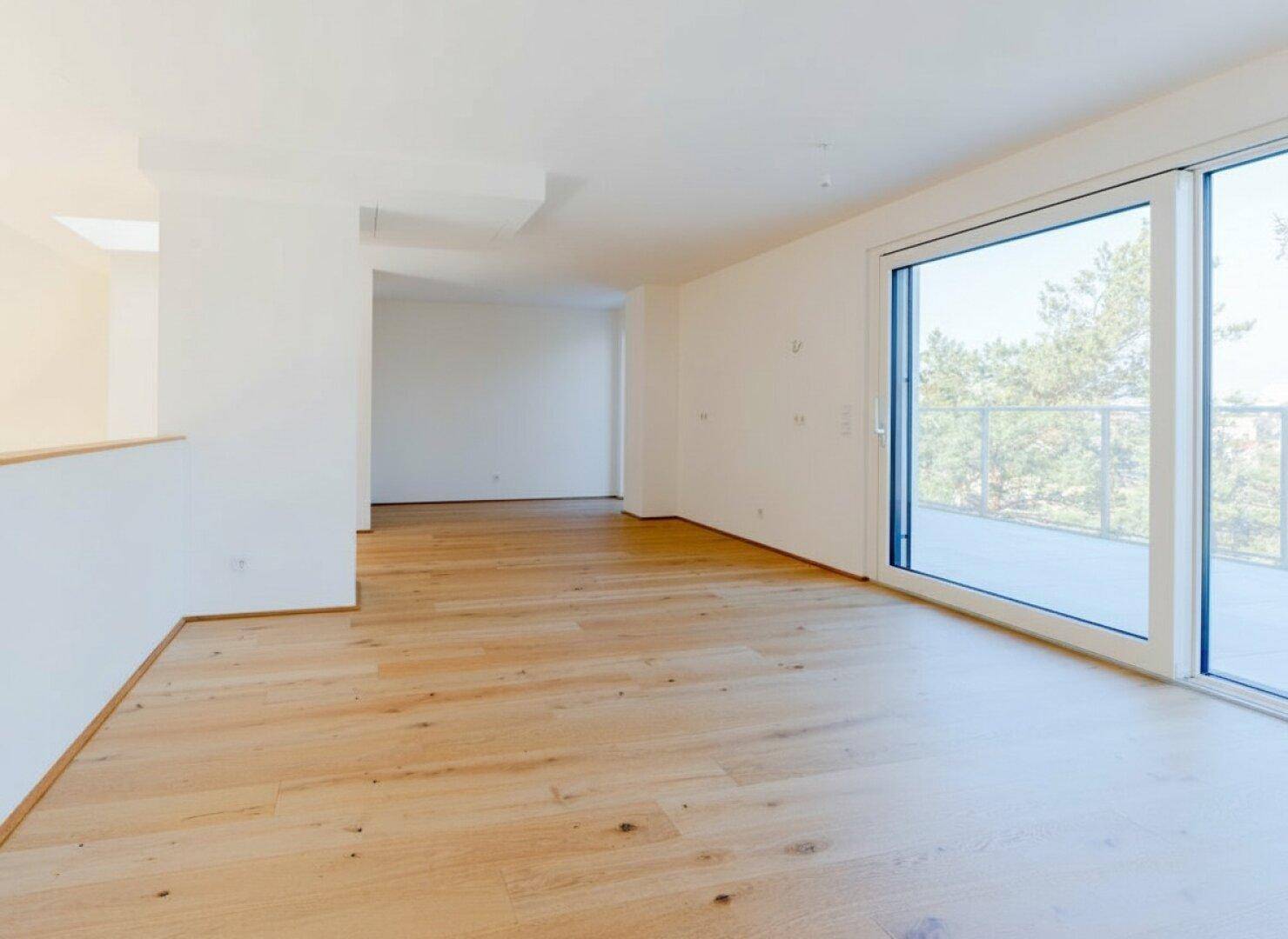 Heller, leerer Raum mit Holzboden und großer Schiebetür, die auf eine Terrasse führt.