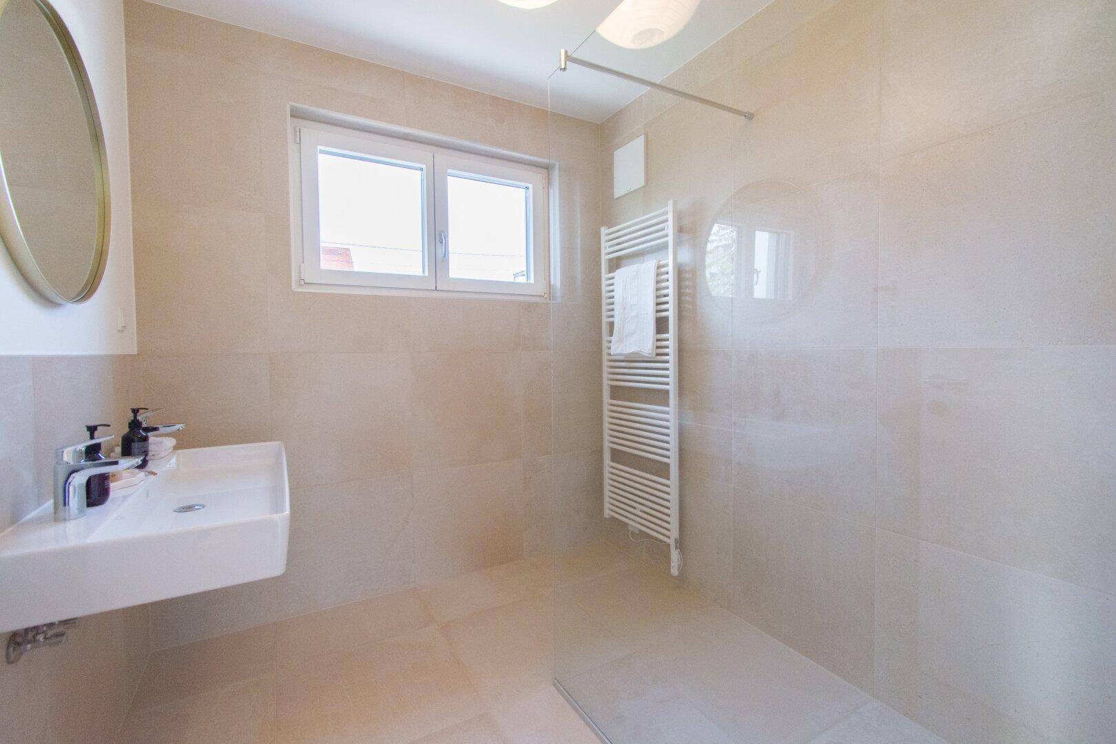Modernes Badezimmer mit ebenerdiger Dusche, Waschbecken und beheiztem Handtuchhalter.