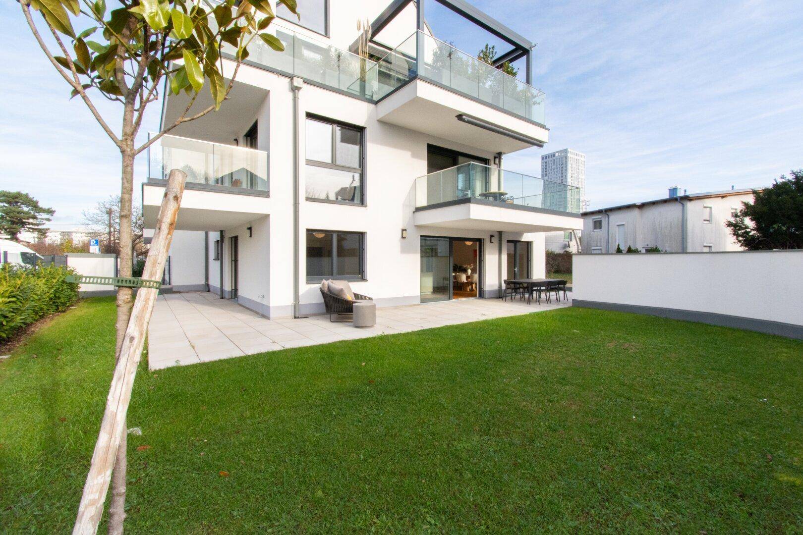 Modernes Mehrfamilienhaus mit gepflegtem Rasen, großer Terrasse und Balkonen.