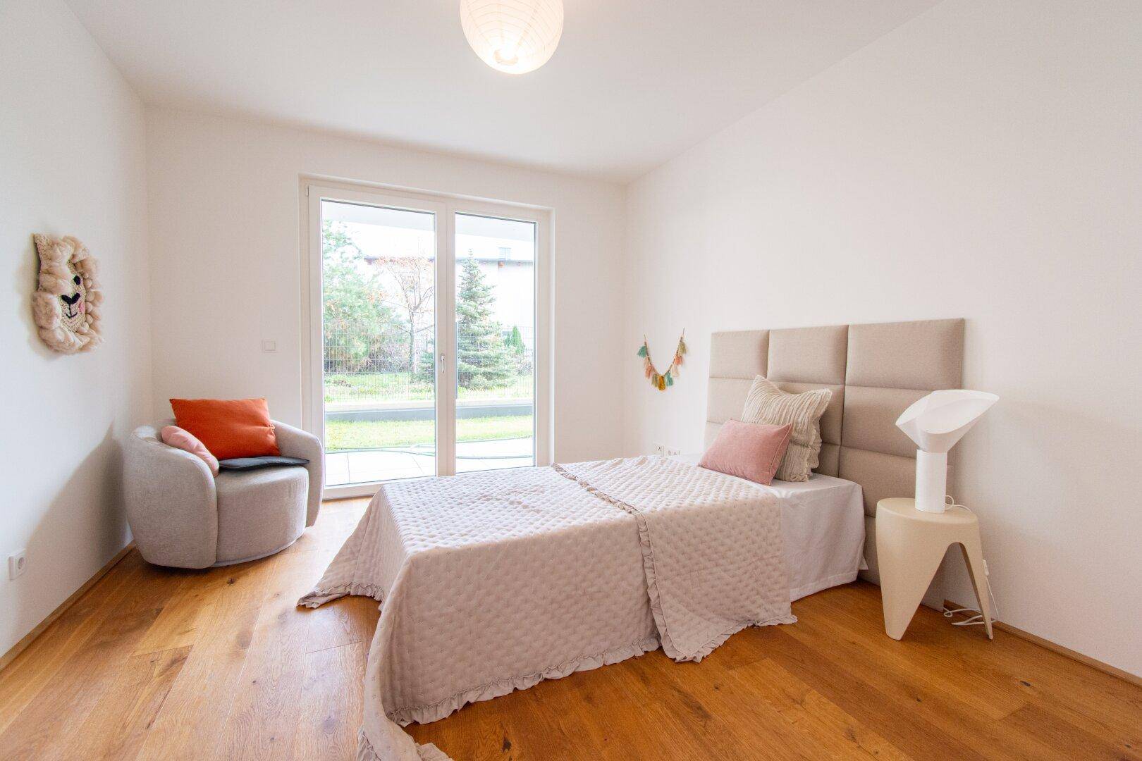 Helles Schlafzimmer mit Holzboden, großem Fenster und Zugang zum Garten.