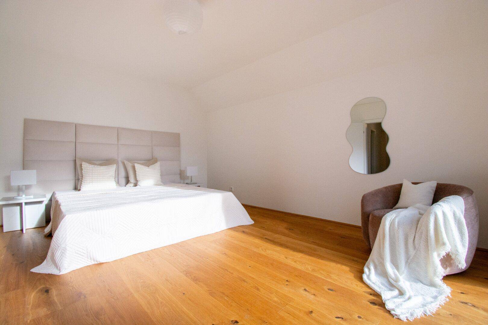 Geräumiges Schlafzimmer mit Holzboden, großem Bett und modernem Sessel.