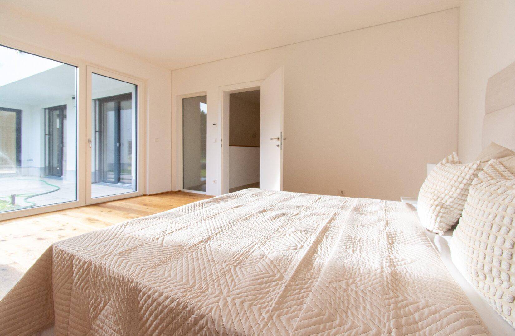 Schlafzimmer mit großem Bett und Zugang zur Terrasse durch bodentiefe Fenster.