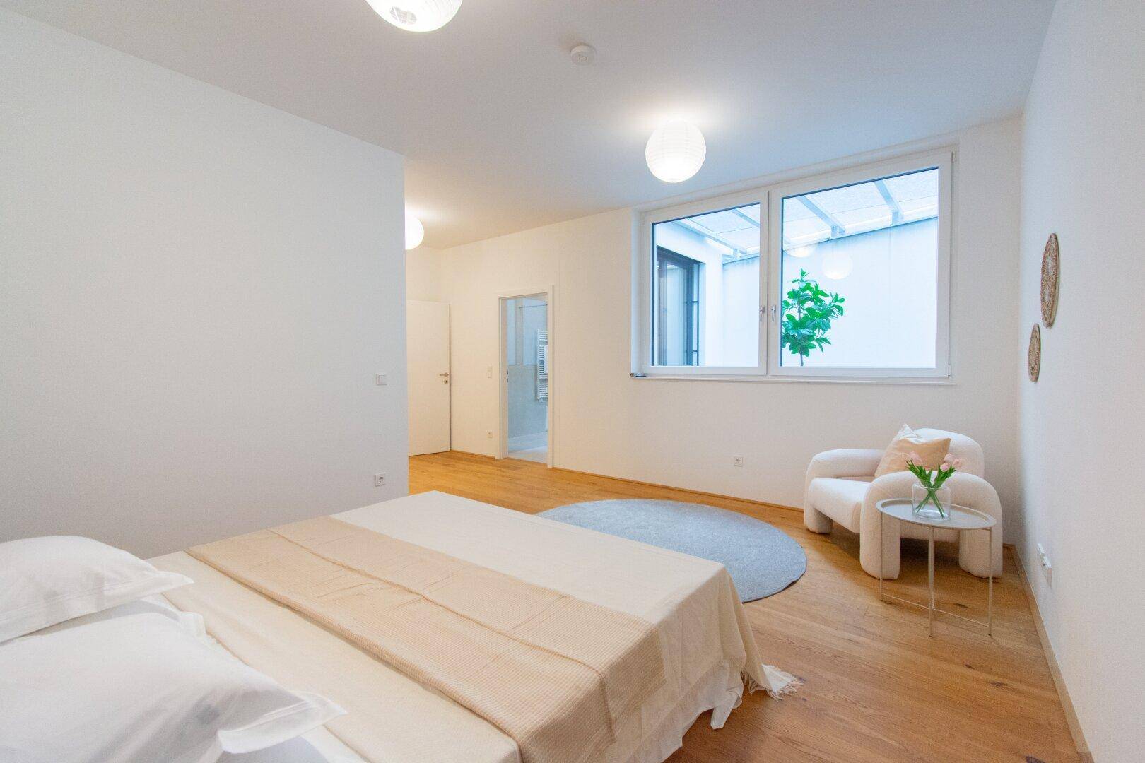 Helles Schlafzimmer mit Holzboden, großem Bett und Blick auf einen Innenhof.