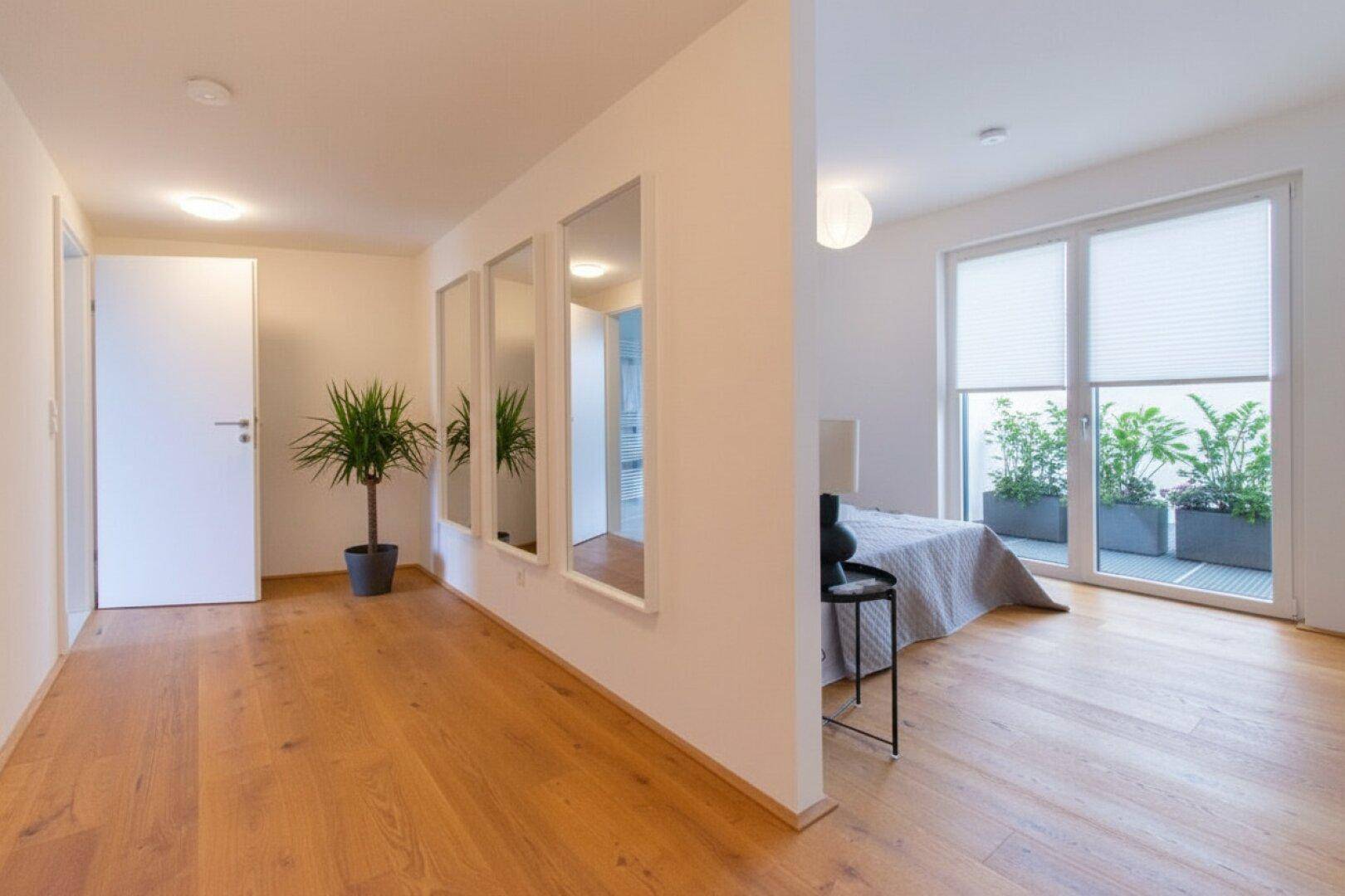 Flur mit Holzboden und Blick in ein Schlafzimmer mit Balkonzugang.