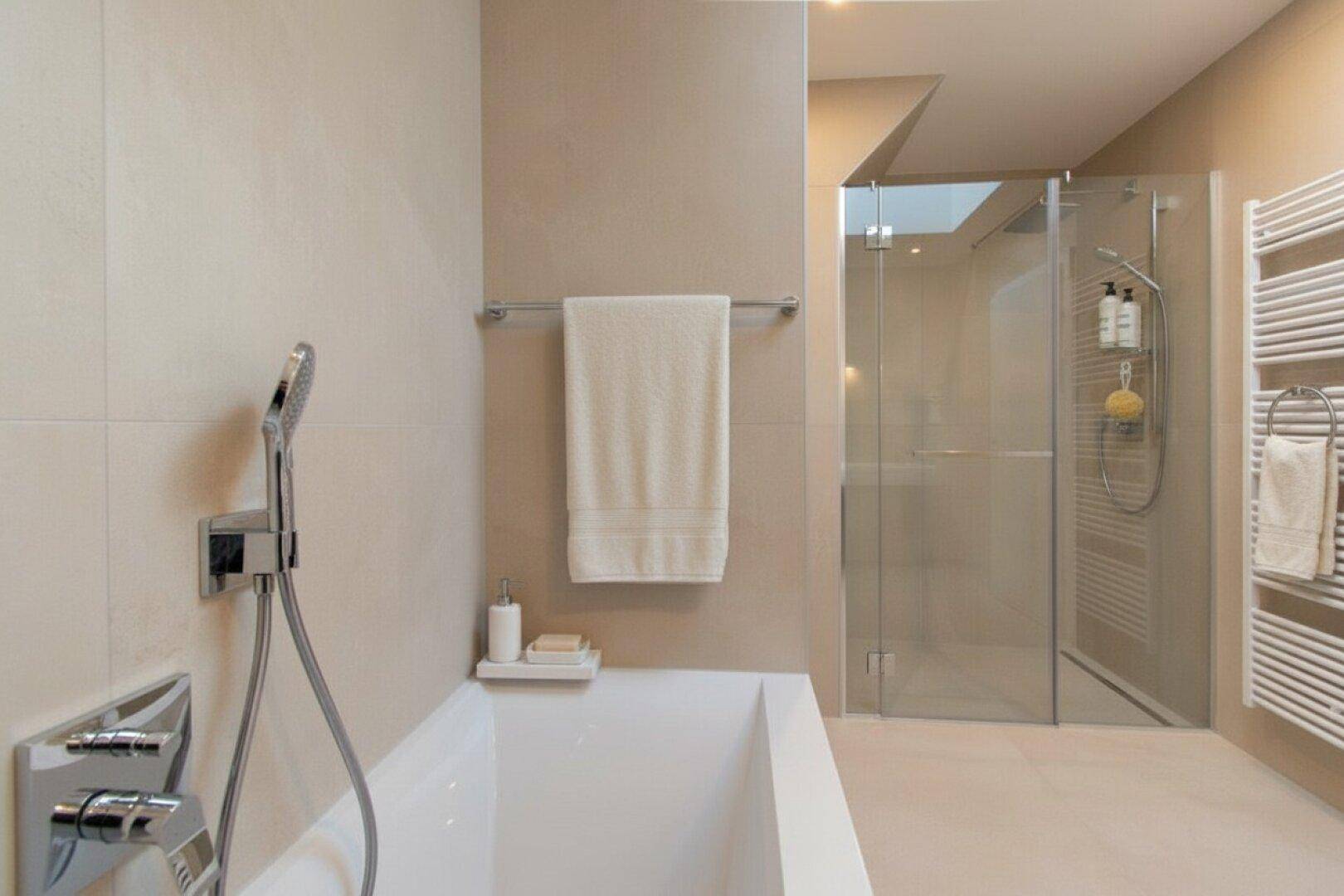 Modernes Badezimmer mit Badewanne, begehbarer Dusche und beheiztem Handtuchhalter in hellen Farbtönen.