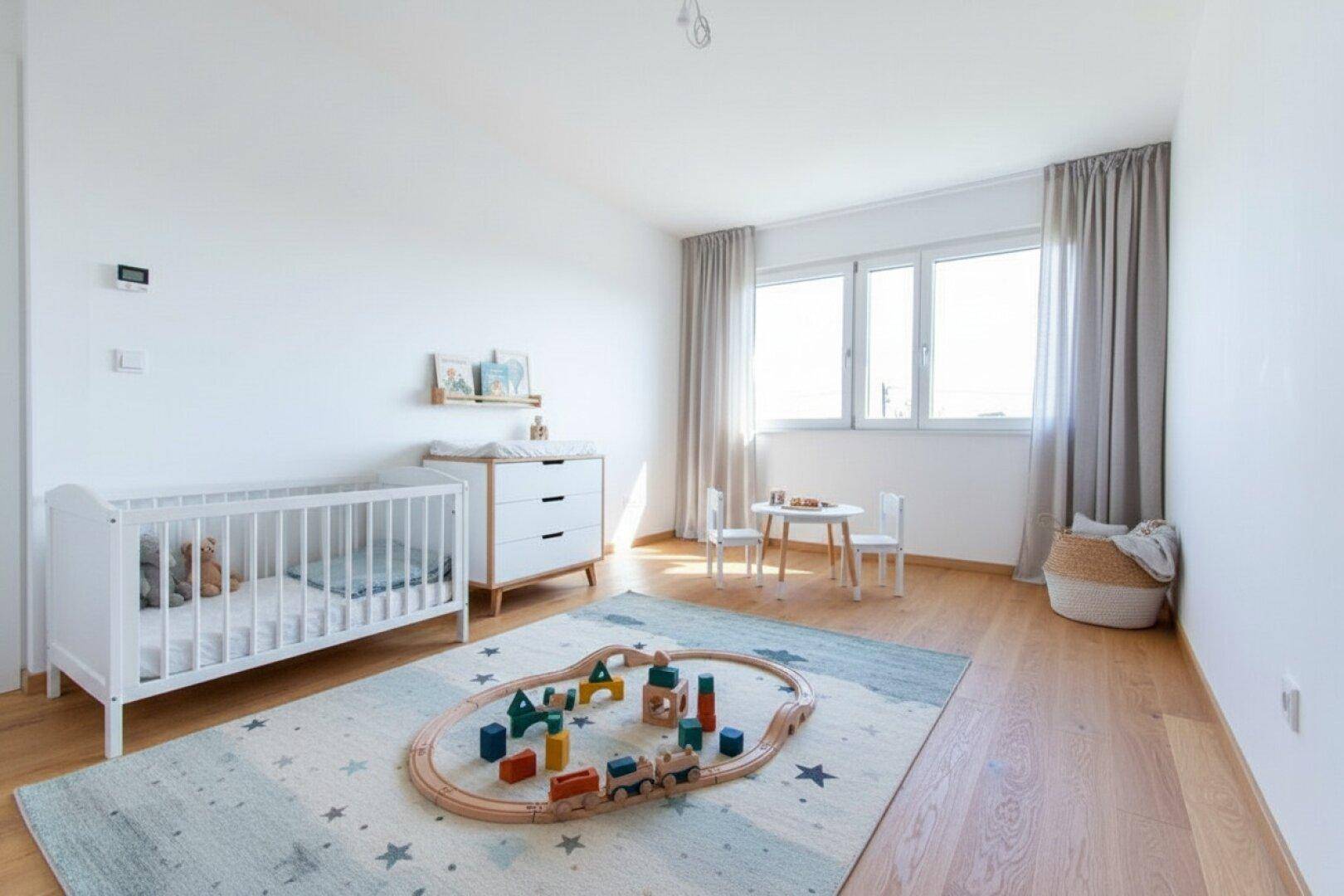 Helles Kinderzimmer mit Holzboden, großem Fenster und Spielbereich für Kleinkinder.