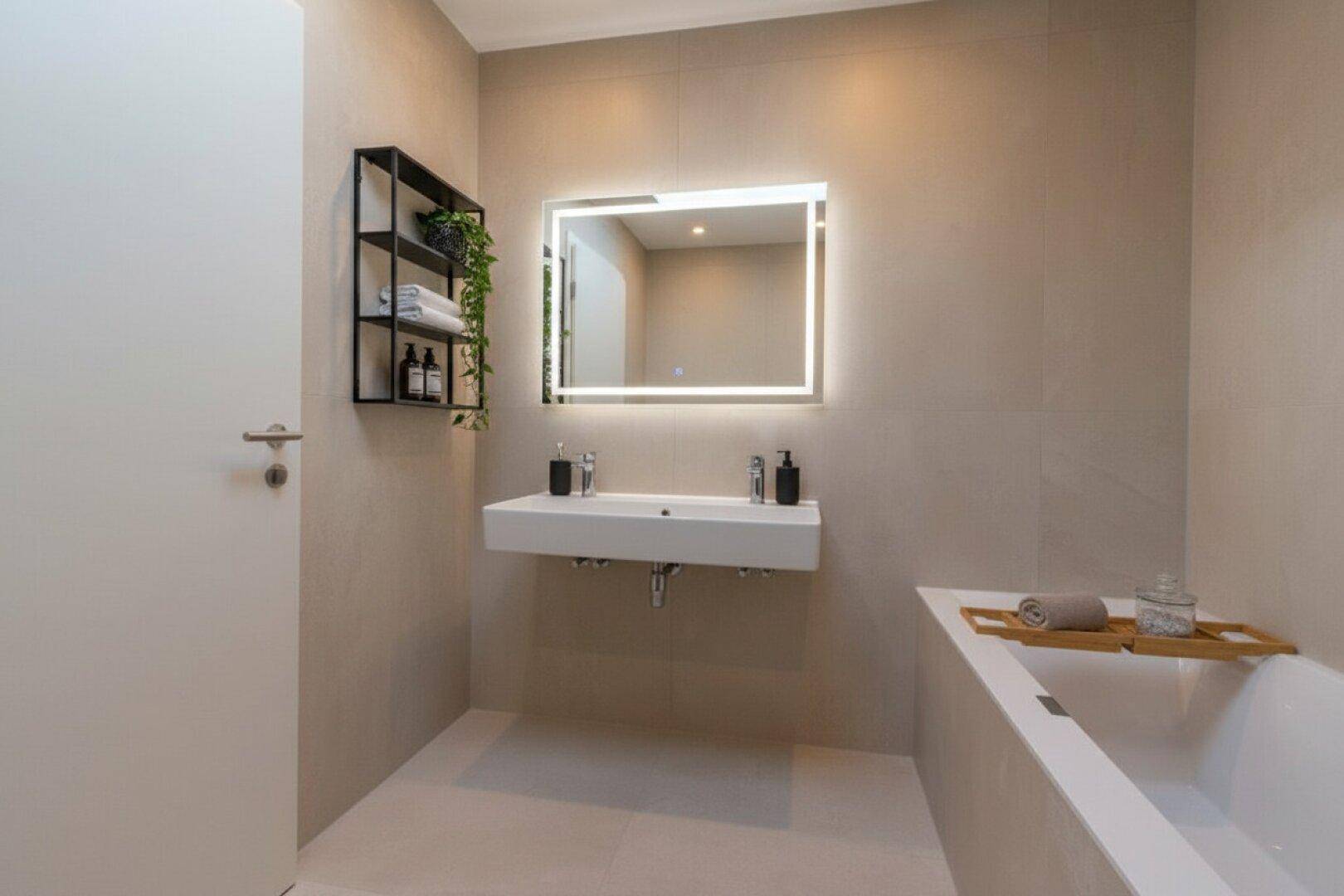 Elegantes Badezimmer mit integrierter Badewanne, Doppelwaschbecken und beleuchtetem Spiegel.