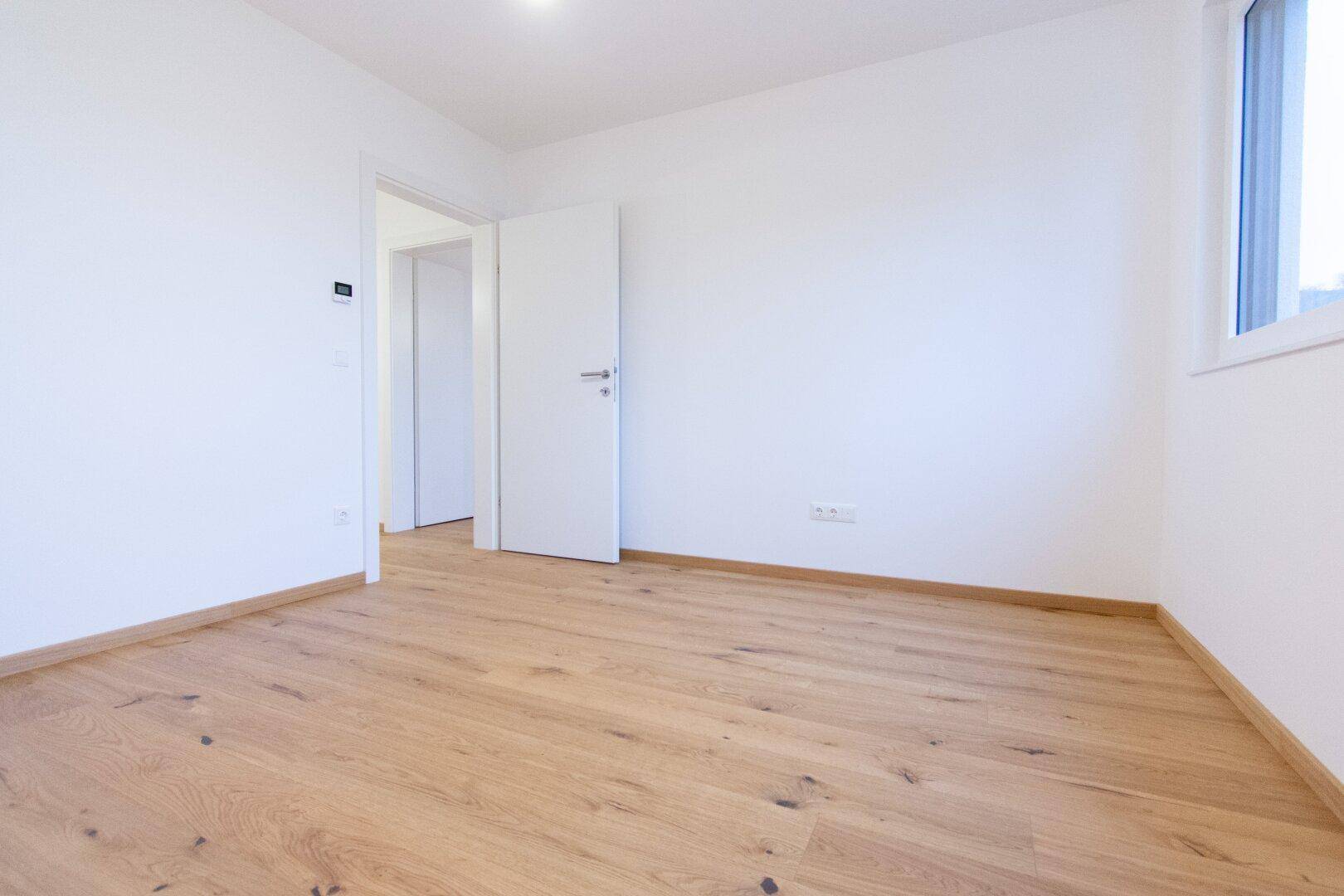 Leeres Schlafzimmer mit hellem Holzparkettboden, weißen Wänden und einem Fenster.