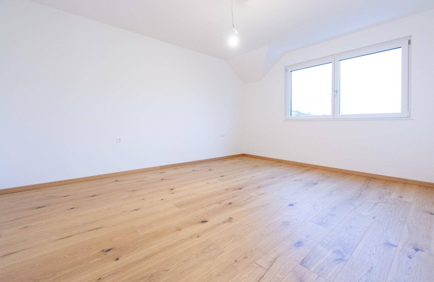 Geräumiges Schlafzimmer im Obergeschoss mit Holzparkettboden und einem großen Fenster.