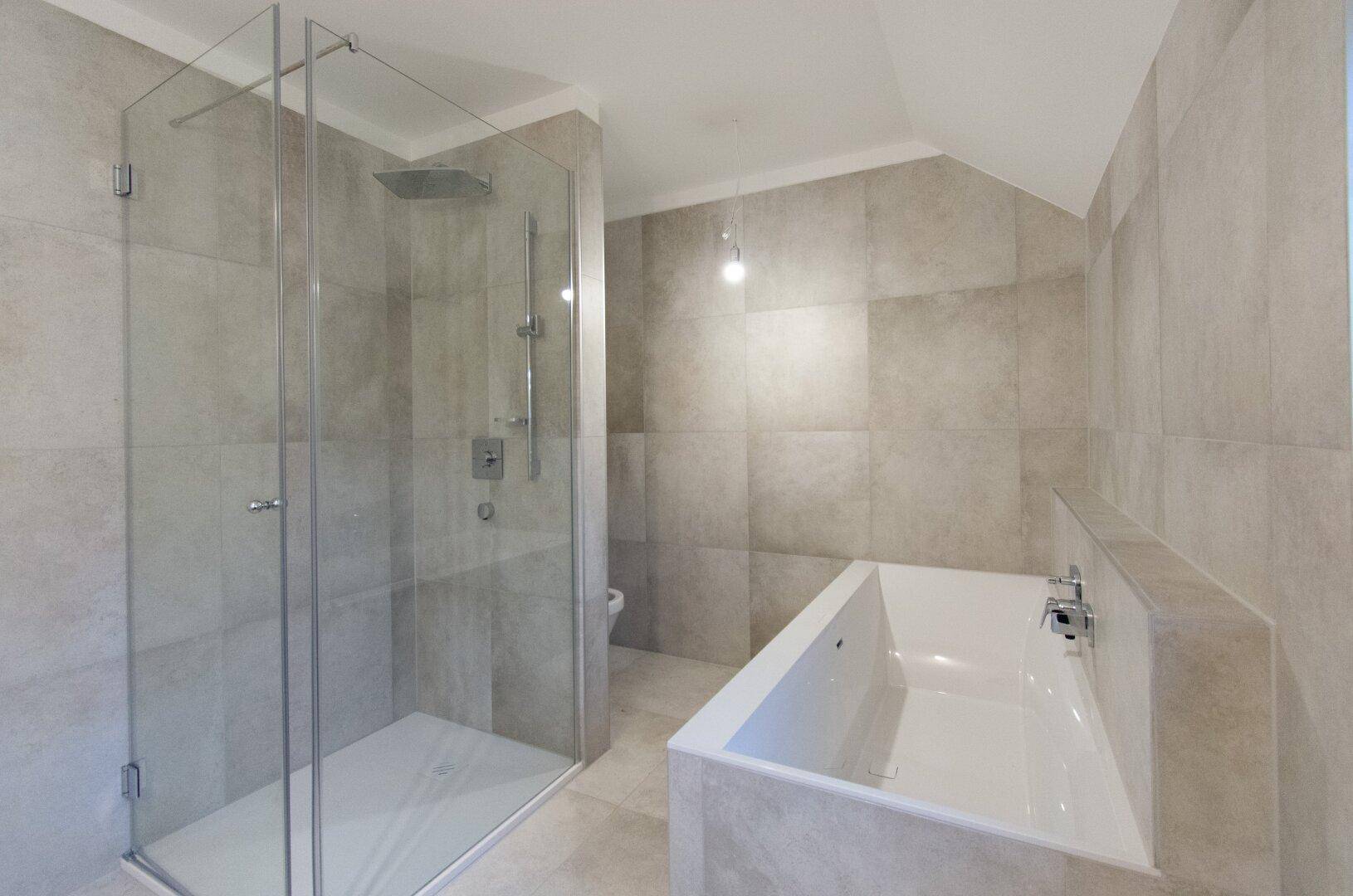 Modernes Badezimmer mit begehbarer Dusche, Badewanne und hellen Fliesen an Wänden und Boden.