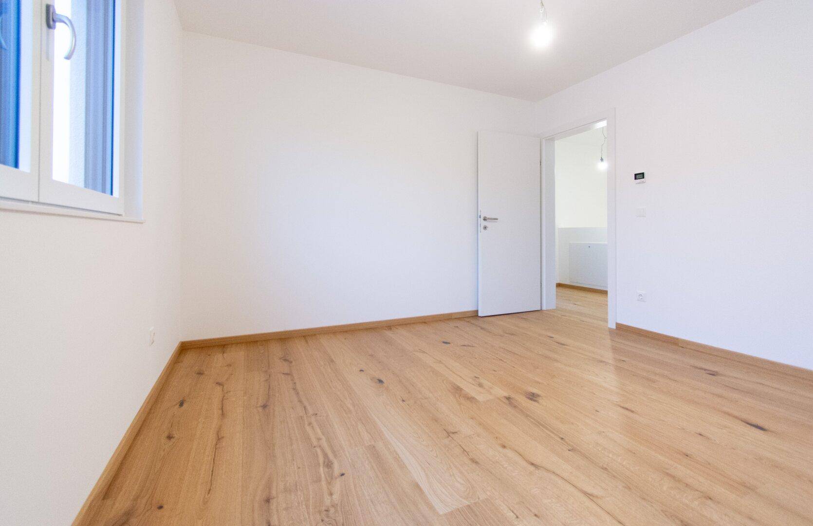 Helles Zimmer mit Holzparkettboden und weiß gestrichenen Wänden, ideal als Schlaf- oder Arbeitszimmer.