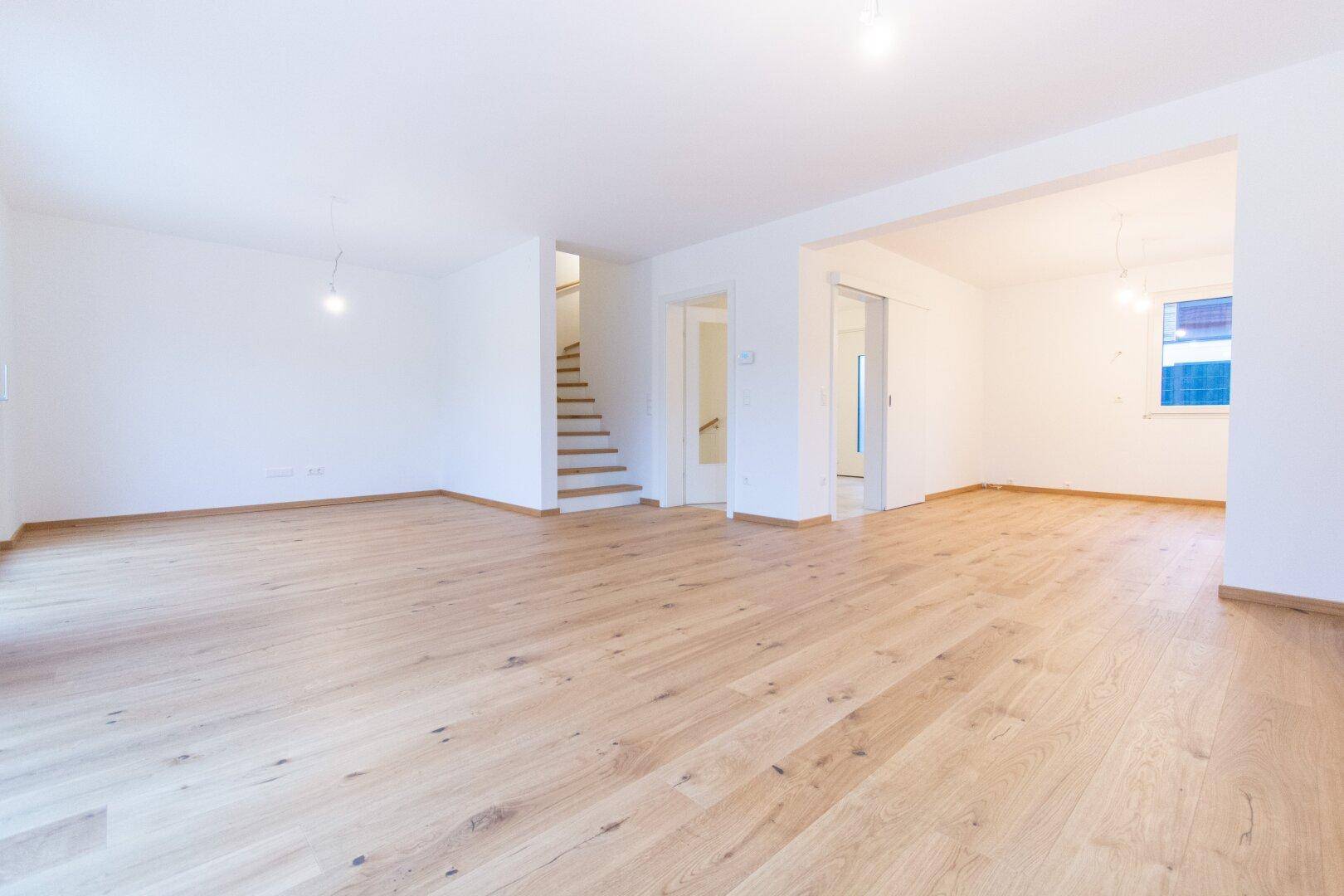 Offener Wohnbereich mit Holzparkettboden, Treppe zum Obergeschoss und viel Tageslicht.