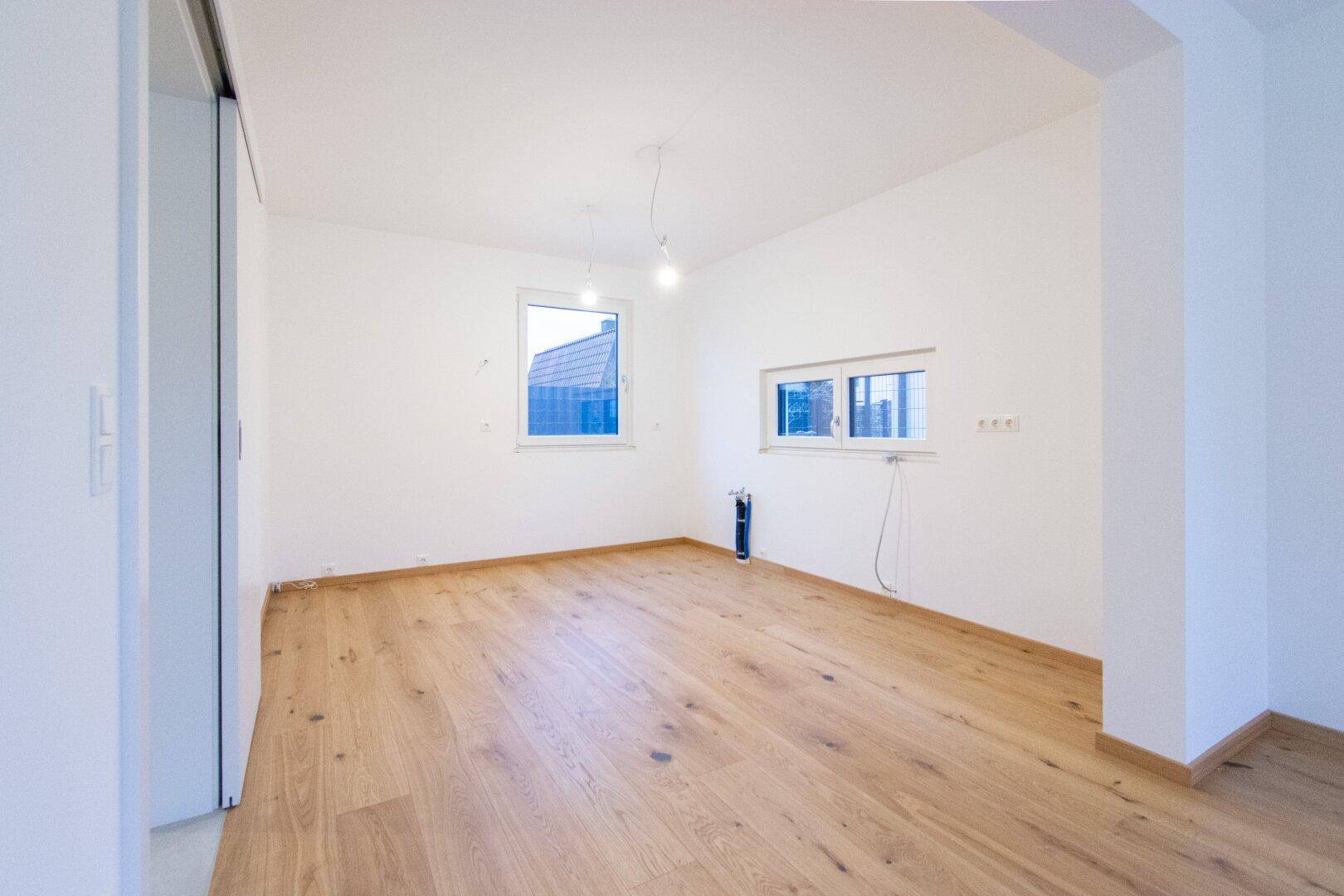 Geräumiges Zimmer mit Holzparkettboden, weißen Wänden und zwei Fenstern für viel Licht.