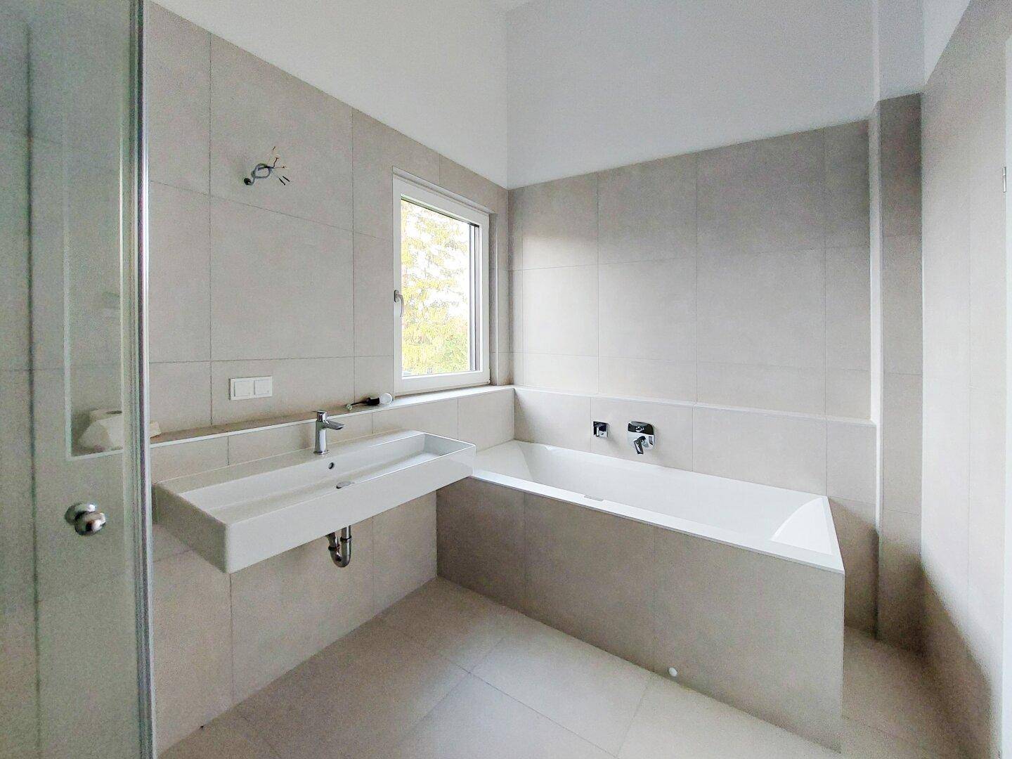Modernes Badezimmer mit Badewanne, Waschtisch und großformatigen Fliesen.