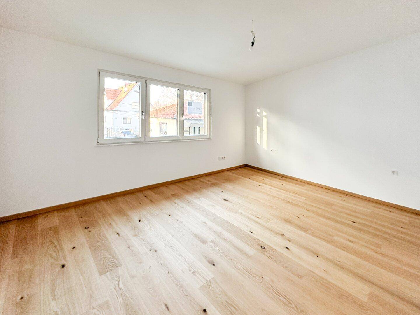 Geräumiges Schlafzimmer mit hellem Holzboden und drei Fenstern für viel Licht.
