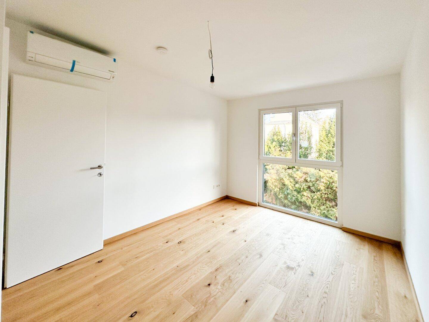 Helles Schlafzimmer mit Holzboden, Klimaanlage und Blick ins Grüne.