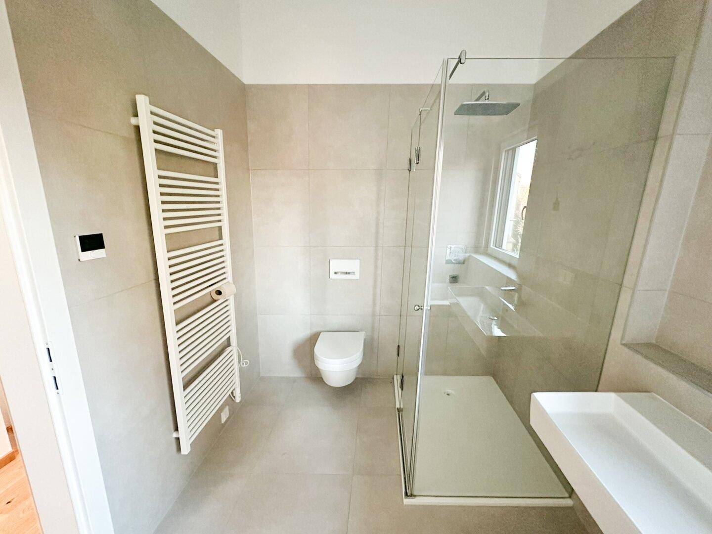 Zeitgemäßes Badezimmer mit ebenerdiger Dusche, Wand-WC und Handtuchheizkörper.