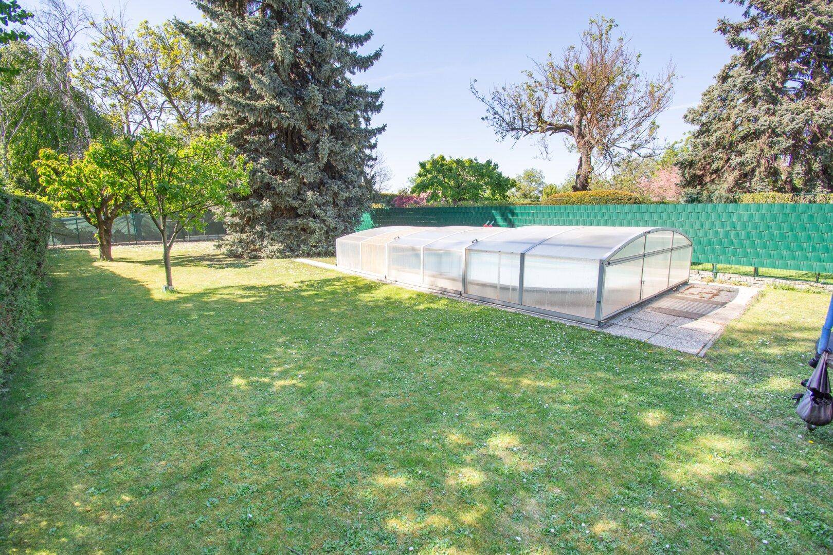 Gepflegter Gartenbereich mit großem, überdachtem Pool und weitläufiger Rasenfläche unter blauem Himmel.