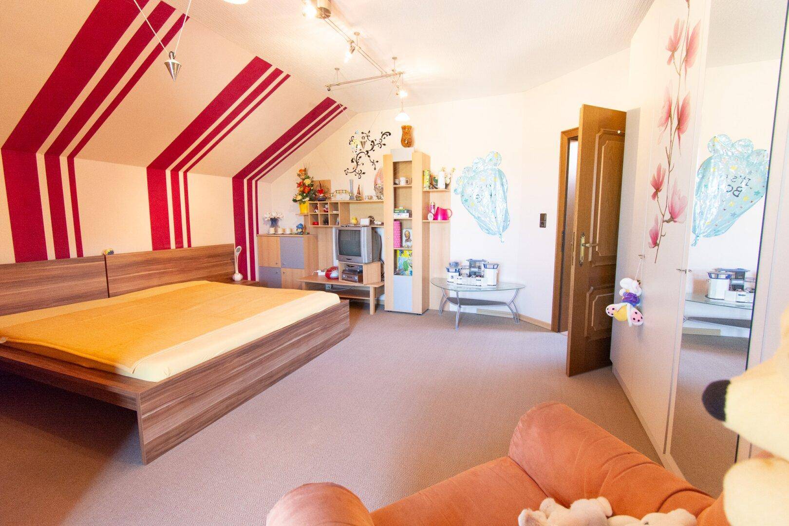 Geräumiges Schlafzimmer im Dachgeschoss mit schrägen Wänden, Teppichboden und farbigen Akzenten.