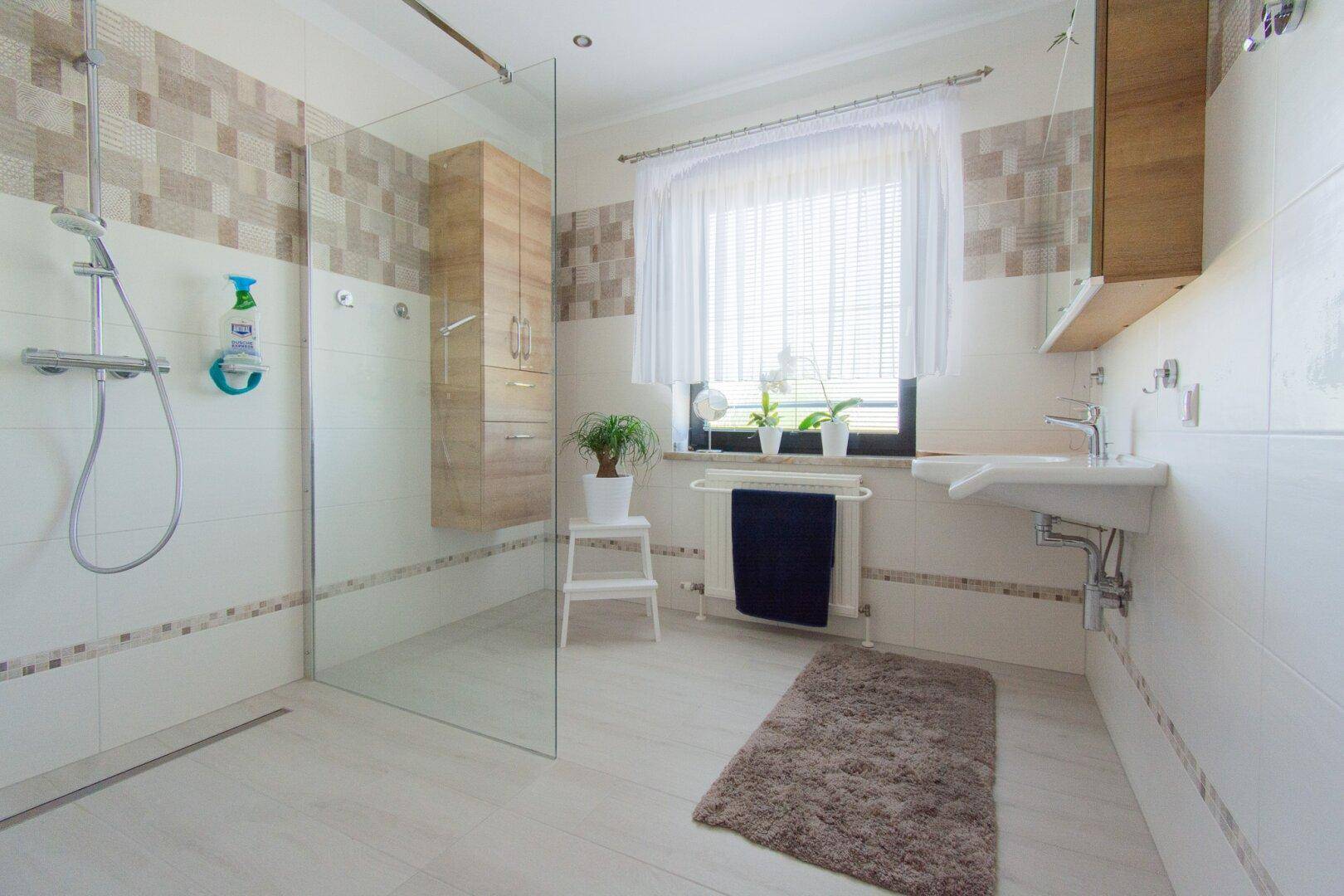 Modernes Badezimmer mit ebenerdiger Dusche, Fenster und hellen Fliesen an Wänden und Boden.