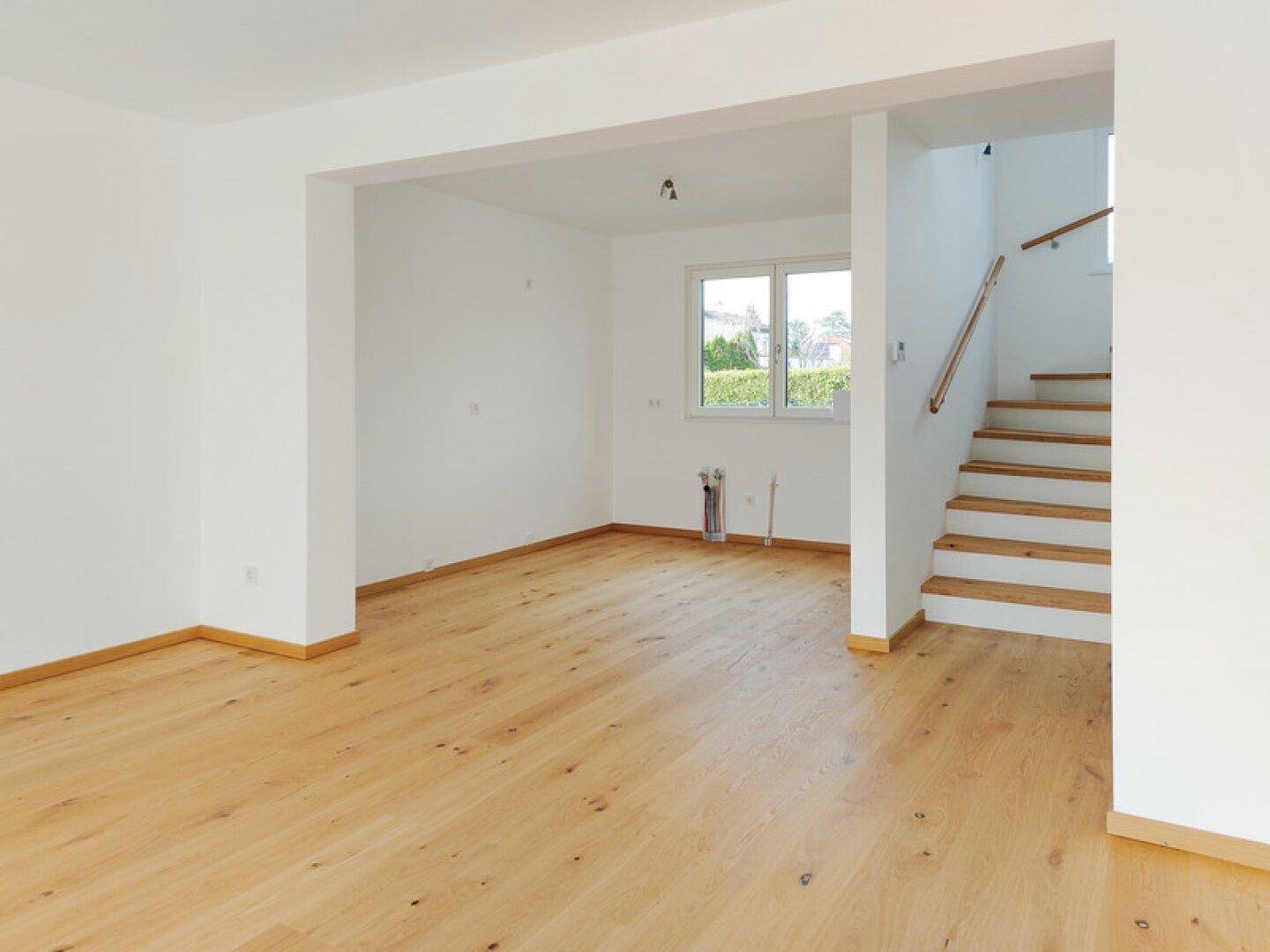 Heller Eingangsbereich mit Holztreppe und Blick in den Garten durch ein Fenster.