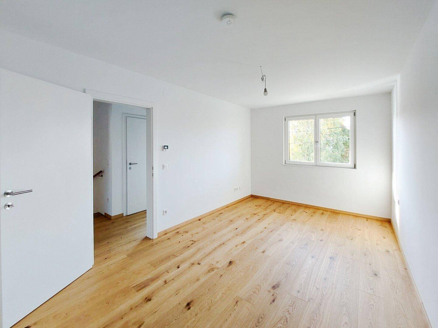 Helles Schlafzimmer mit Holzparkettboden und Fenster, bereit zur individuellen Gestaltung.