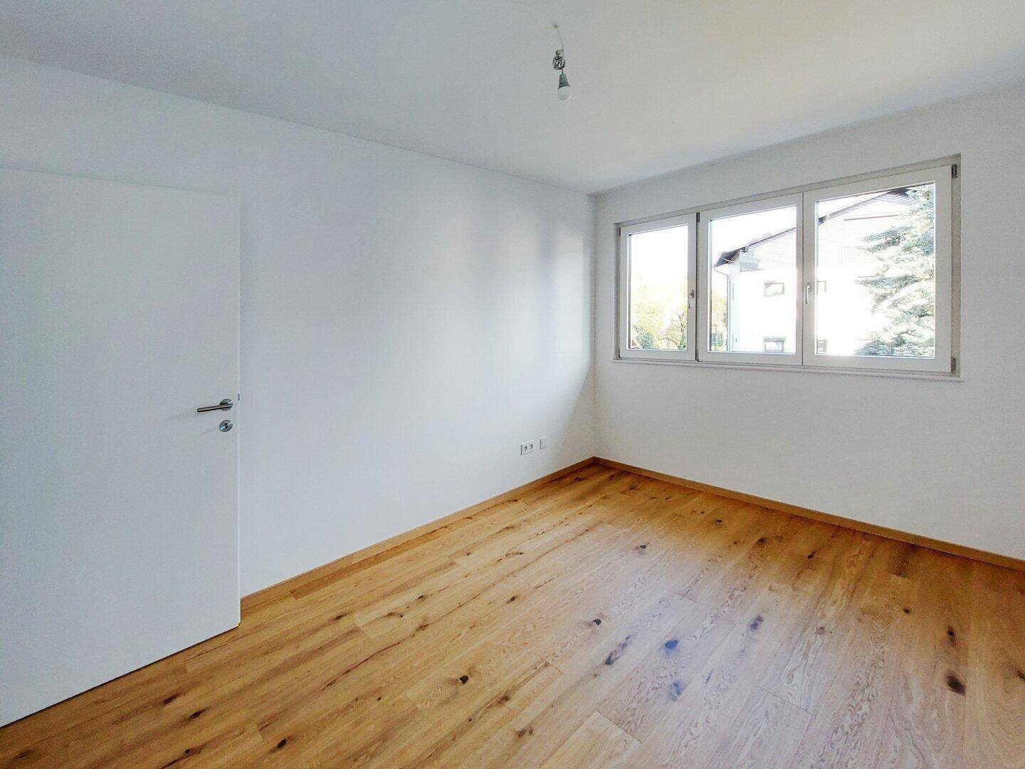 Geräumiges Zimmer mit Holzparkettboden und drei Fenstern für viel natürliches Licht.