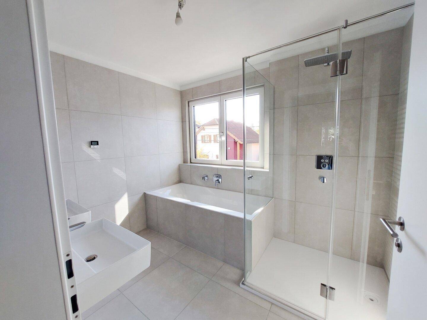 Helles Badezimmer mit Badewanne, Glasdusche und modernem Waschbecken.