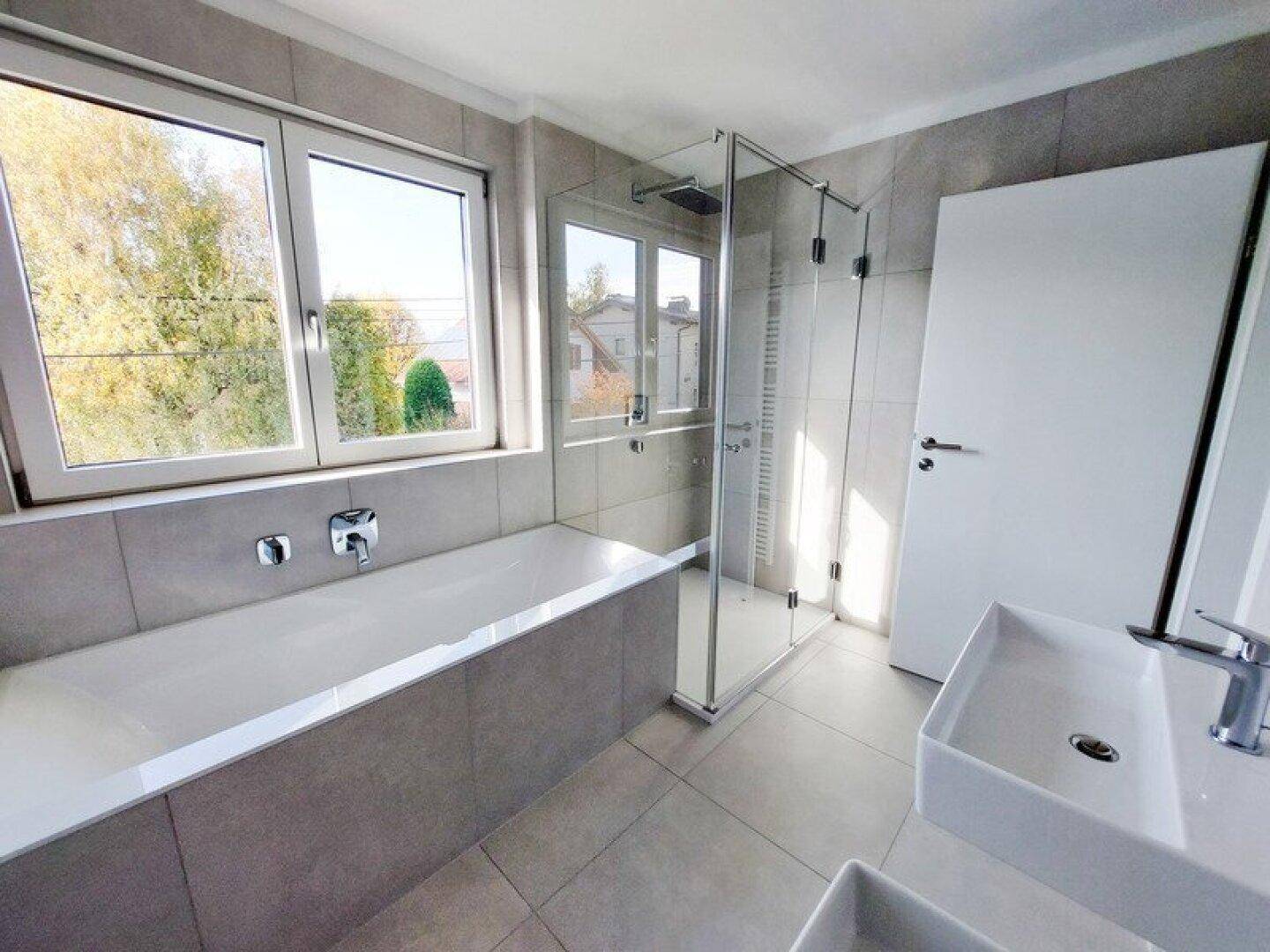 Modernes Badezimmer mit Badewanne, ebenerdiger Dusche und zwei Fenstern.