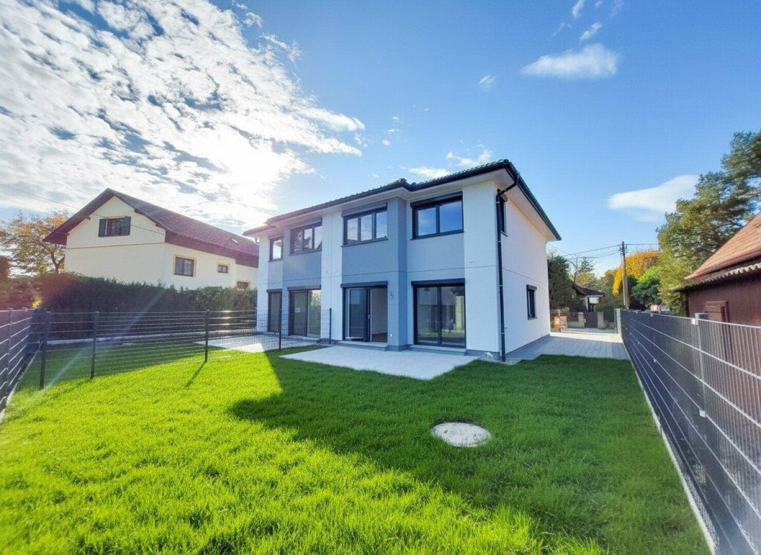 Modernes Doppelhaus mit weißer und grauer Fassade, großem Garten und sonniger Terrasse.