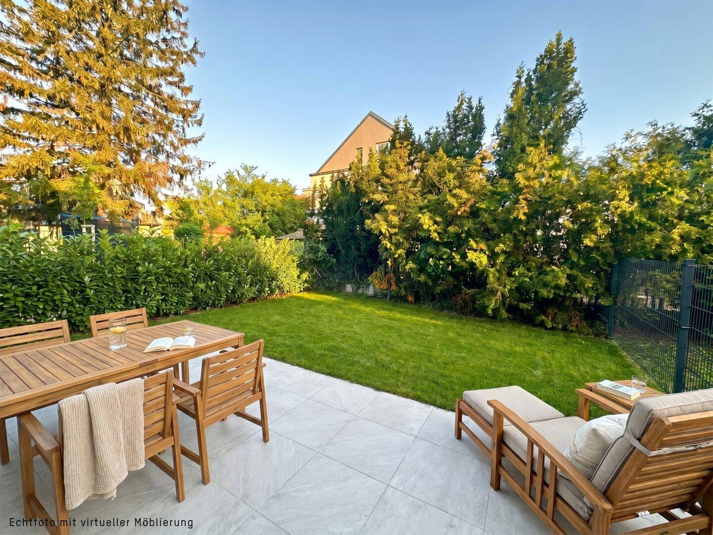 Große geflieste Terrasse mit Holzmöbeln, angrenzendem Rasen und umgeben von hohen Bäumen.