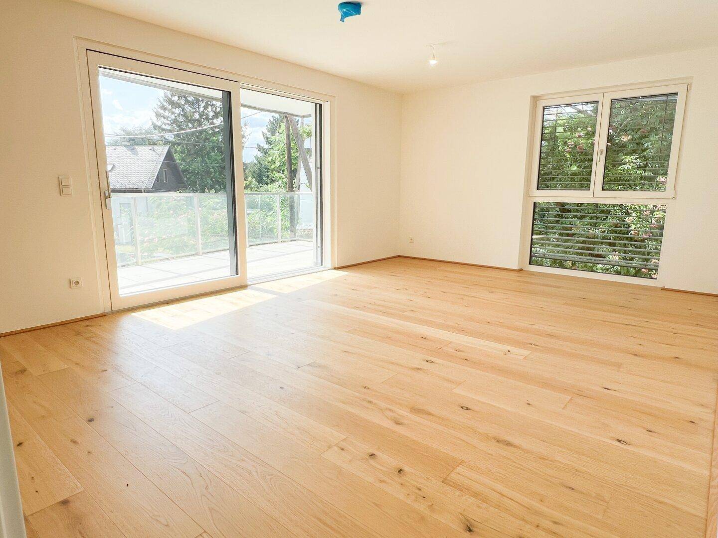 Geräumiger, heller Raum mit großen Schiebetüren zum Balkon und hellem Holzfußboden.