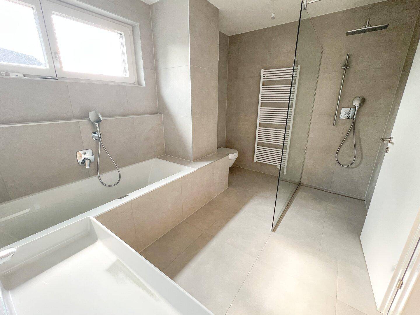 Modernes Badezimmer mit Badewanne, ebenerdiger Dusche, beheiztem Handtuchhalter und Fenster.